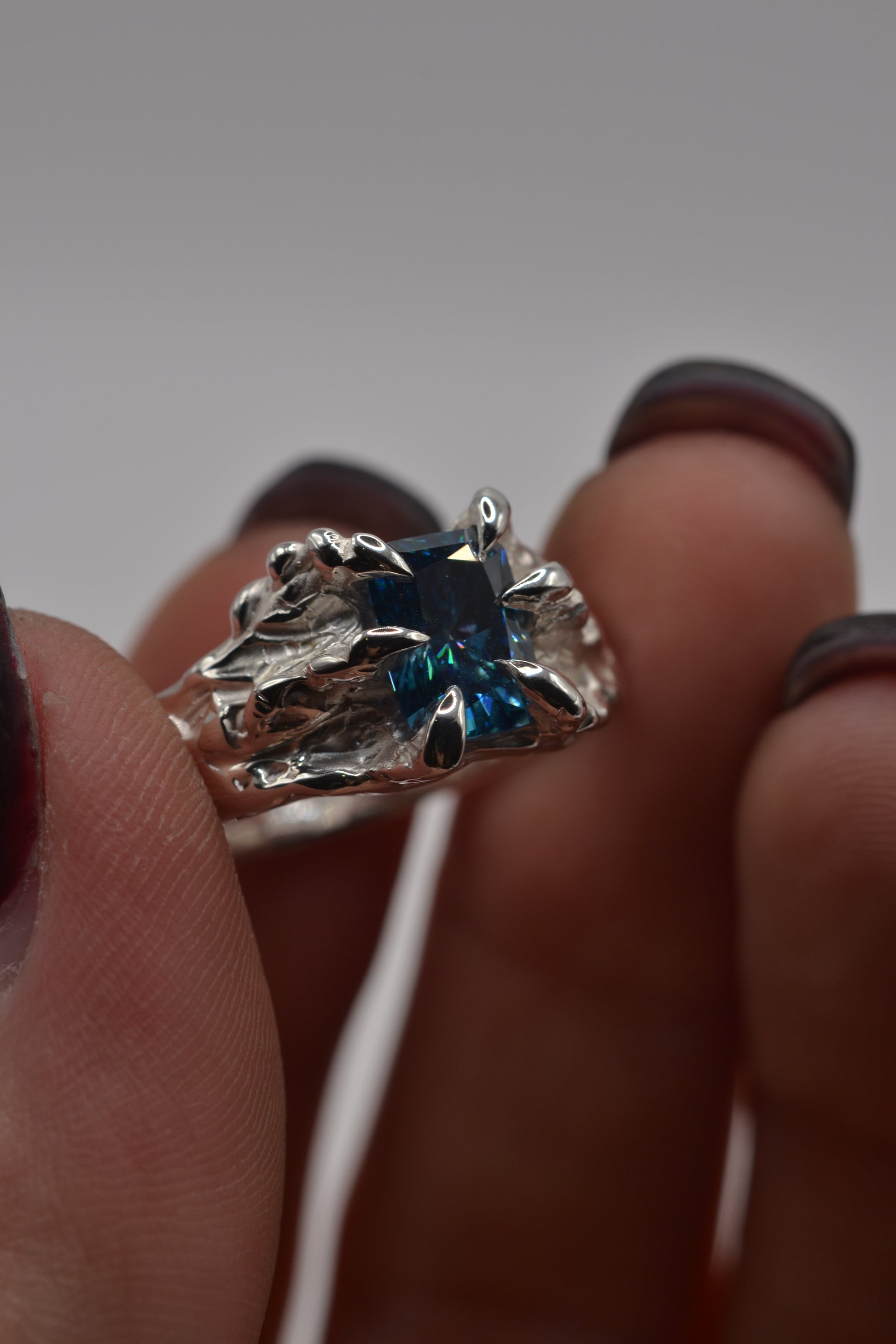 Close-up of a handmade alternative silver ring with a blue radiant cut moissanite, formed using traditional lost wax casting.