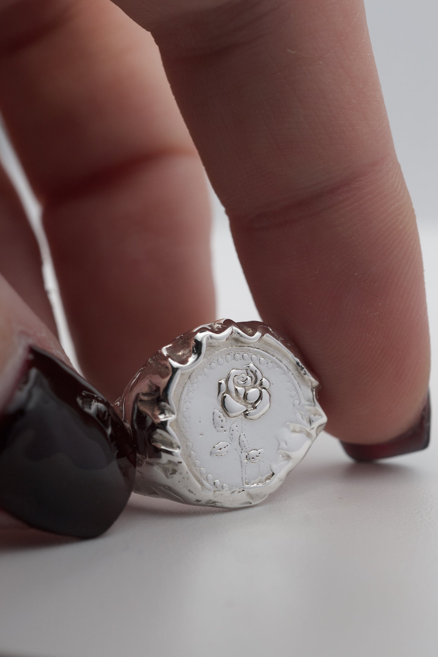 Close-up detail of a handmade lost wax silver ring showing the raised embossed rose motif and textured molten edge finish.