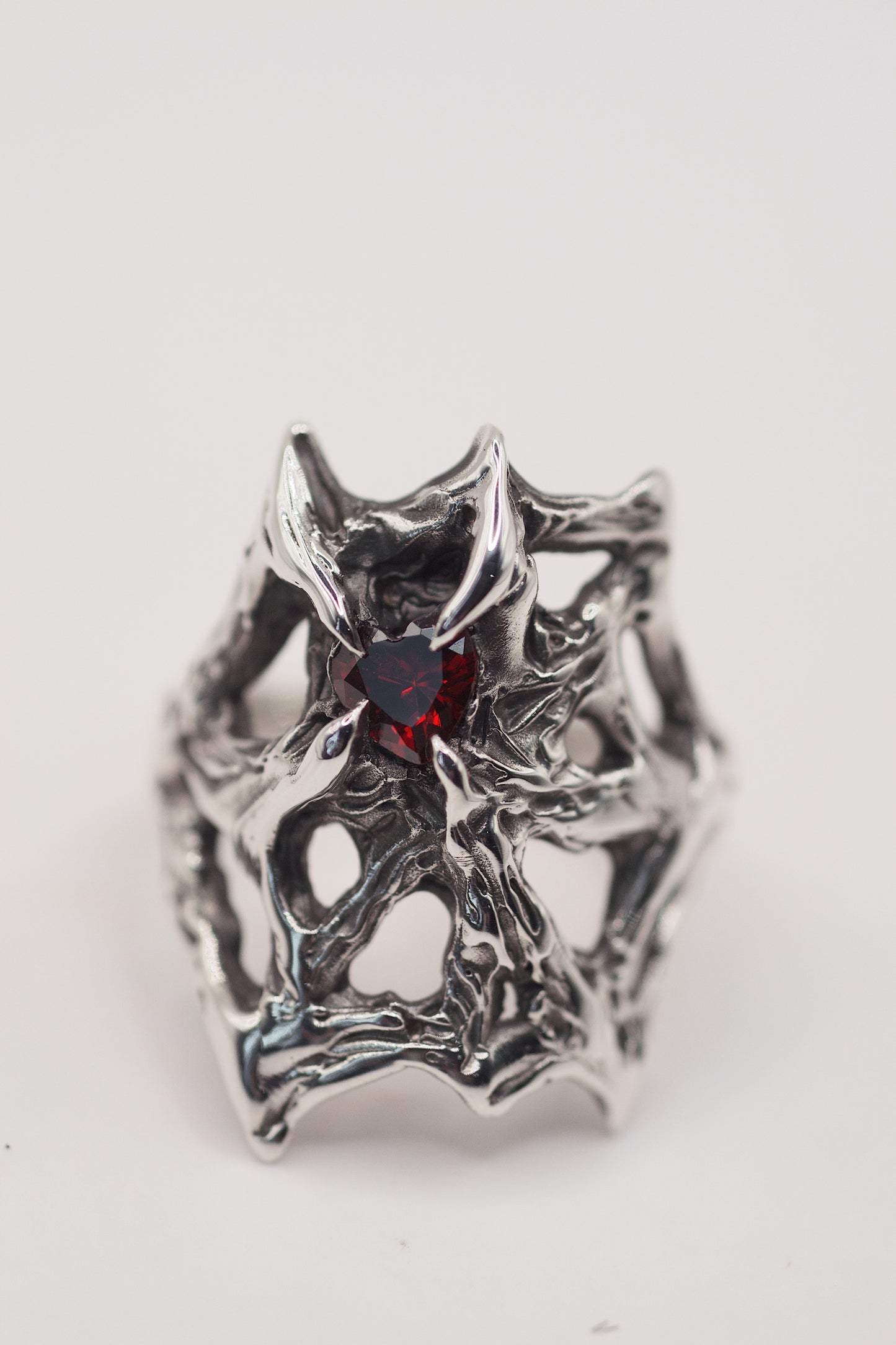 gothic web engagement ring with high polish, and a red heart shape garnet stone. Handmade using the lost wax technique. Recycled eco friendly 925 sterling silver. Alternative designs and a high quality ring front view. Grunge jewellery.