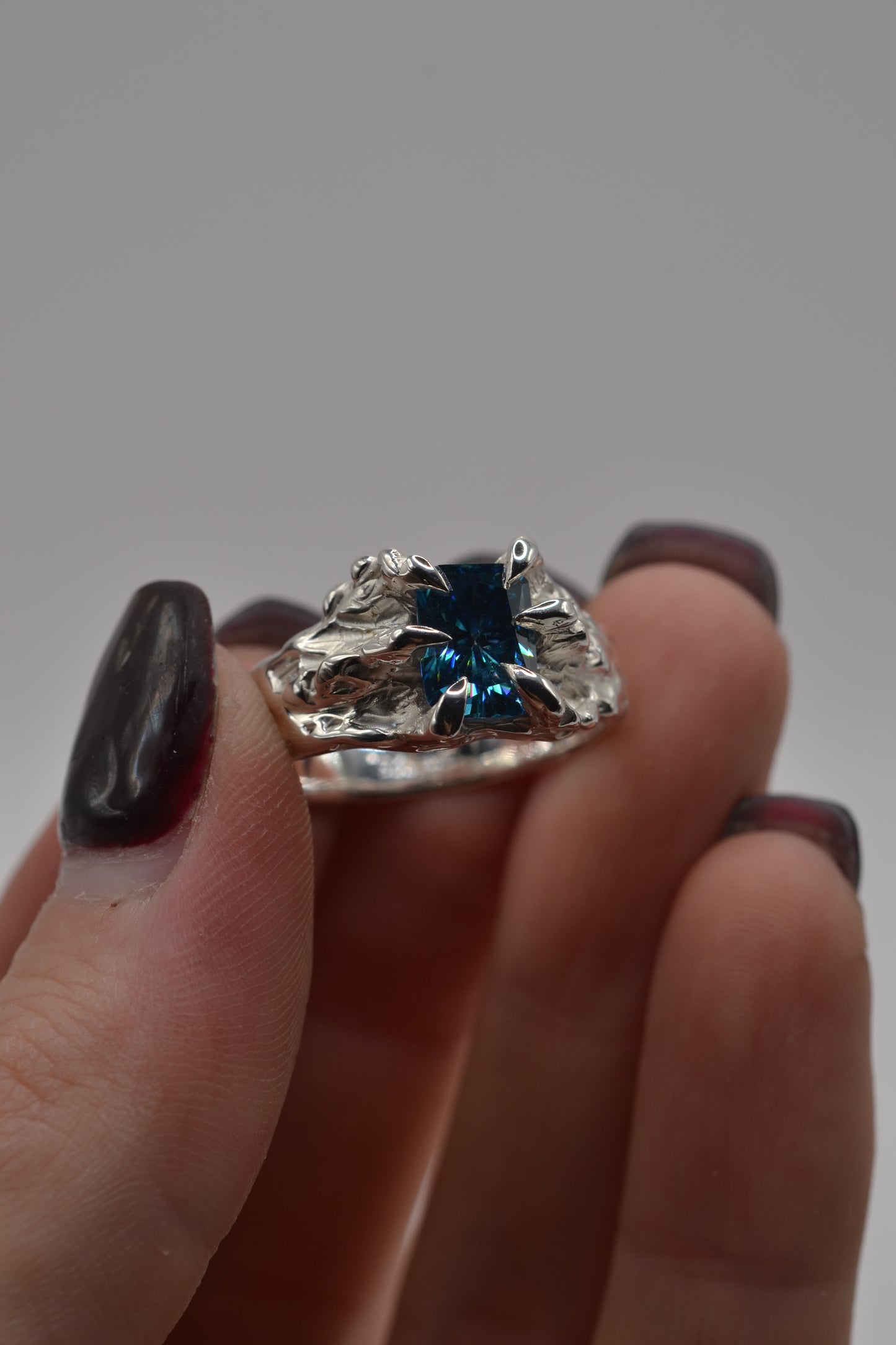 Detailed view of a lost wax cast silver ring with a blue radiant cut moissanite, showcasing organic textures and claw setting.