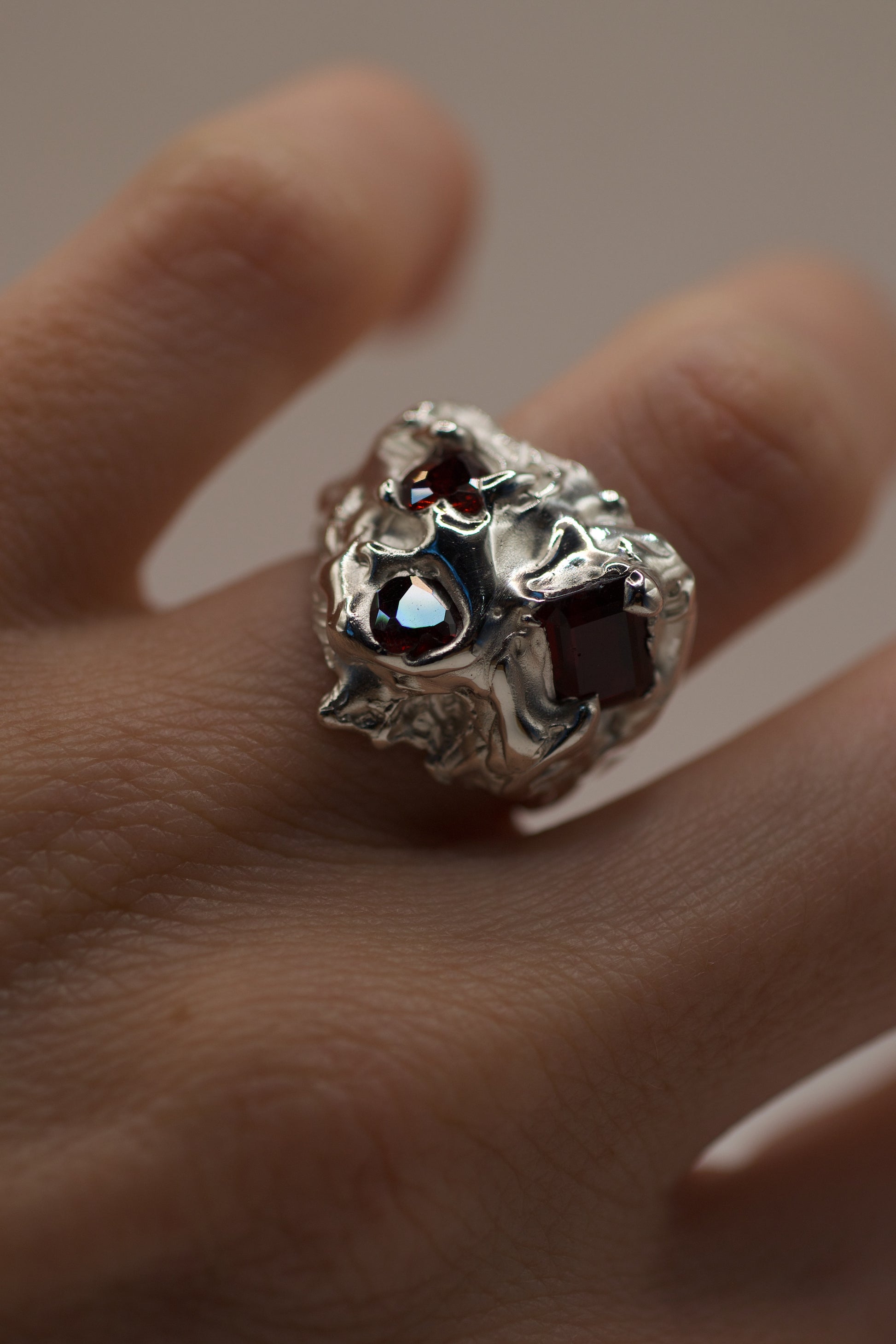 Silver ring with gemstones on a finger against a neutral background