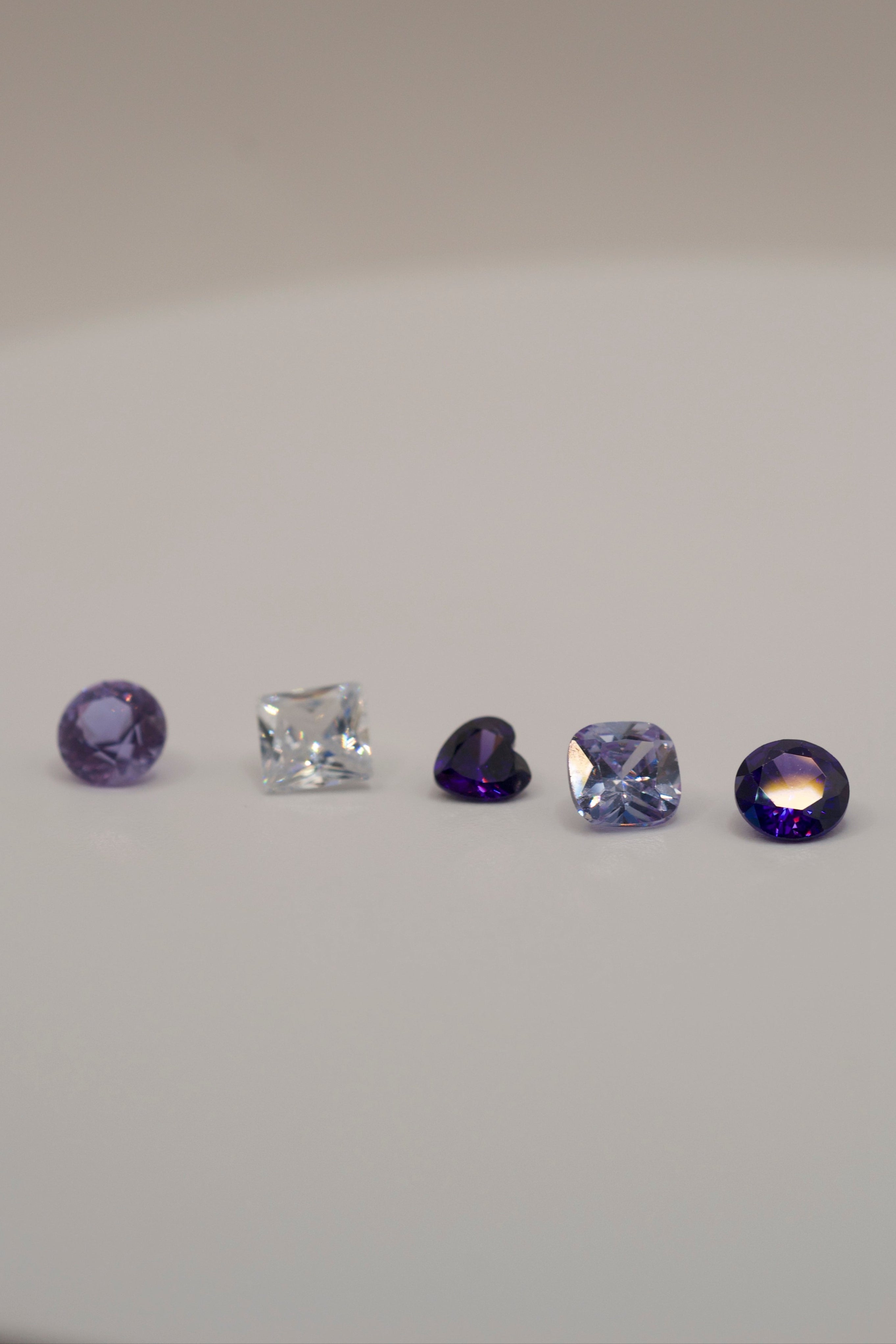 Loose gemstones for lost wax casting and cast in place jewelry — purple, violet, and clear faceted stones in round, heart, cushion, and princess cuts.