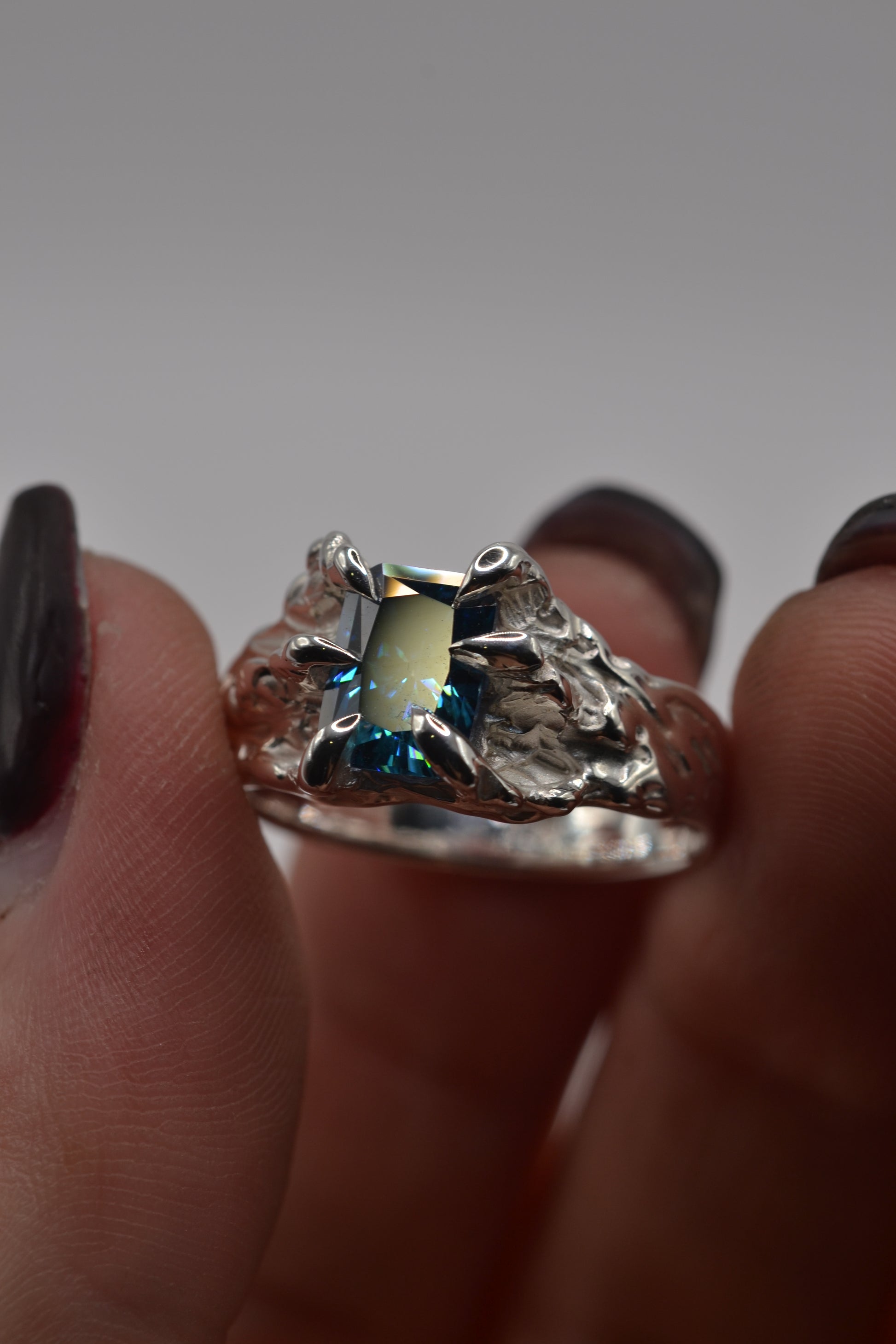 Front view of a lost wax silver ring featuring a blue radiant cut moissanite, designed in an organic alternative style.