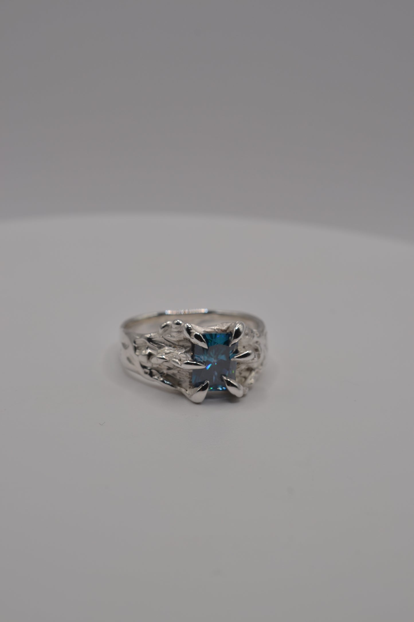 Front-facing view of a handmade lost wax silver ring featuring a blue radiant cut moissanite in an organic setting.