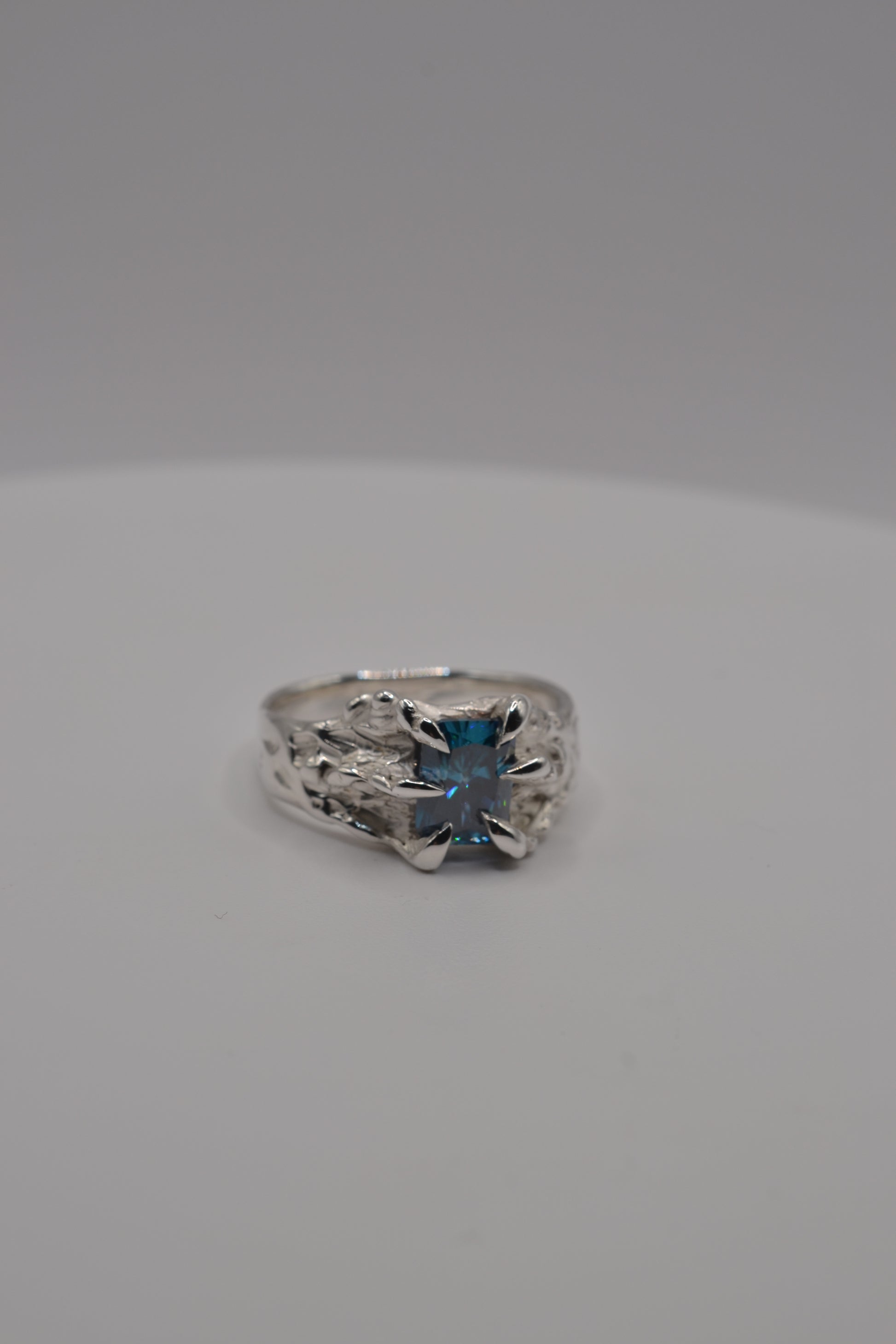 Front-facing view of a handmade lost wax silver ring featuring a blue radiant cut moissanite in an organic setting.