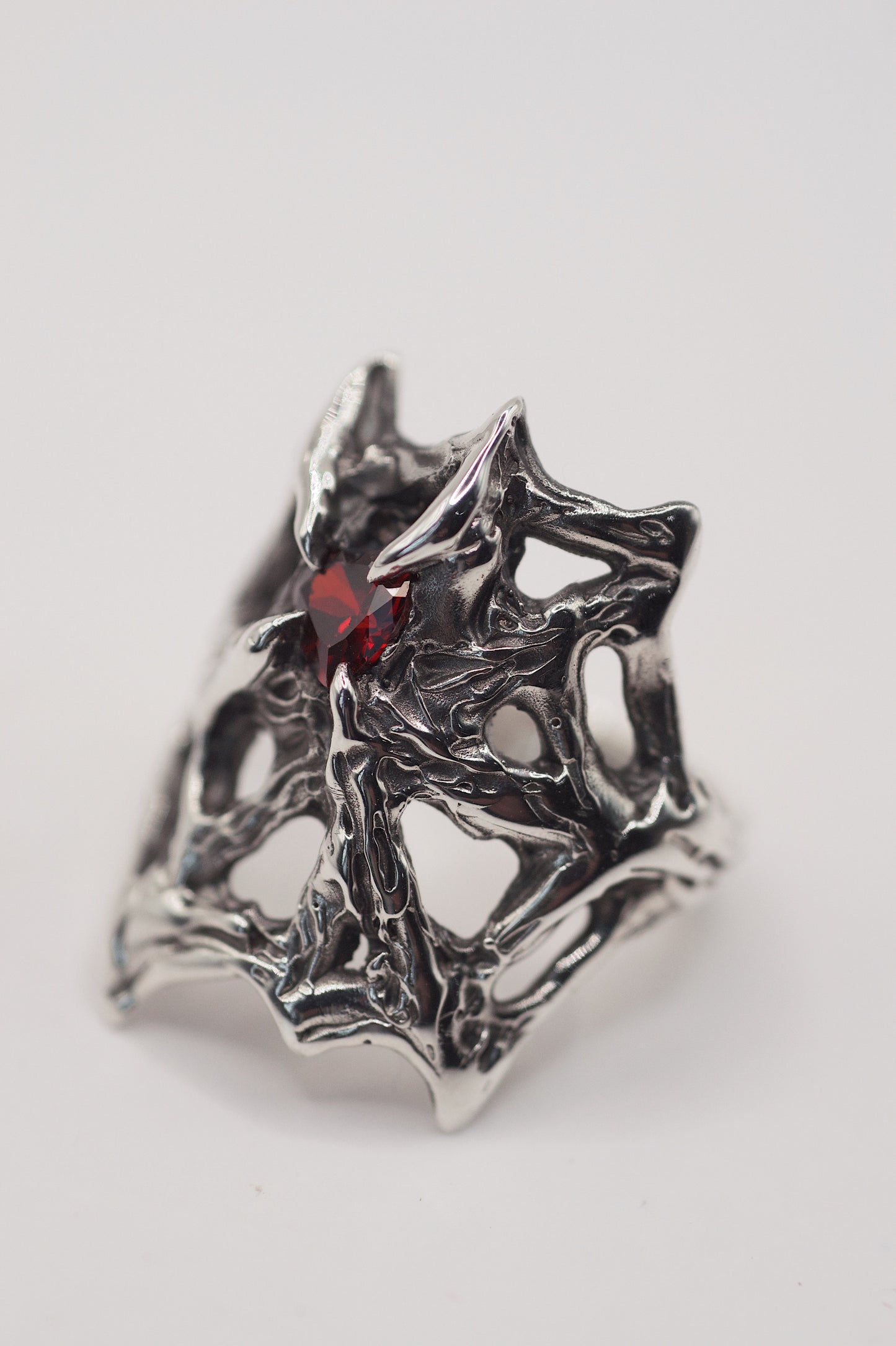 gothic web engagement ring with high polish, and a red heart shape garnet stone. Handmade using the lost wax technique. Recycled eco friendly 925 sterling silver. Alternative designs and a high quality ring front view. Grunge jewellery.