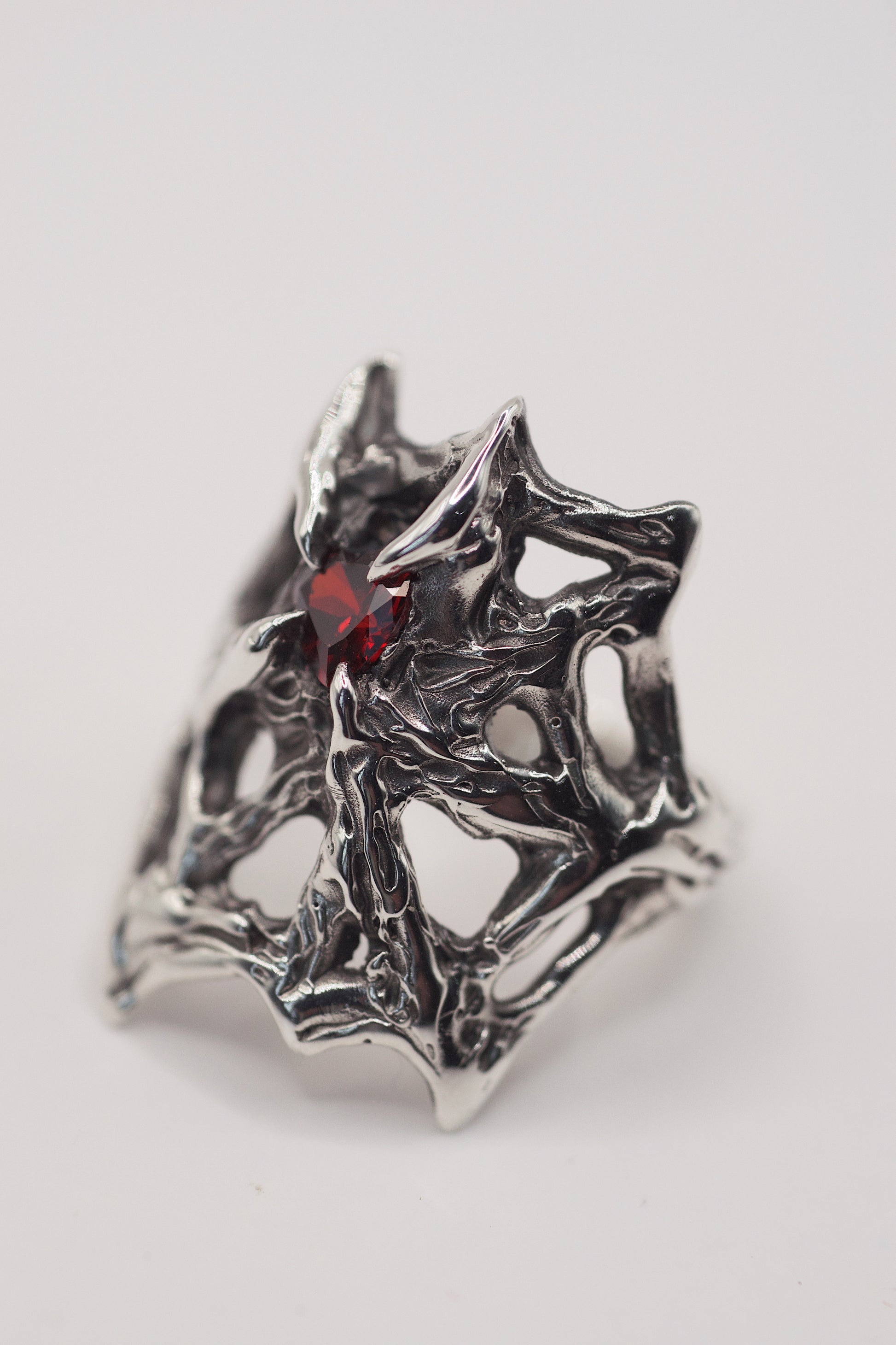 gothic web engagement ring with high polish, and a red heart shape garnet stone. Handmade using the lost wax technique. Recycled eco friendly 925 sterling silver. Alternative designs and a high quality ring front view. Grunge jewellery.