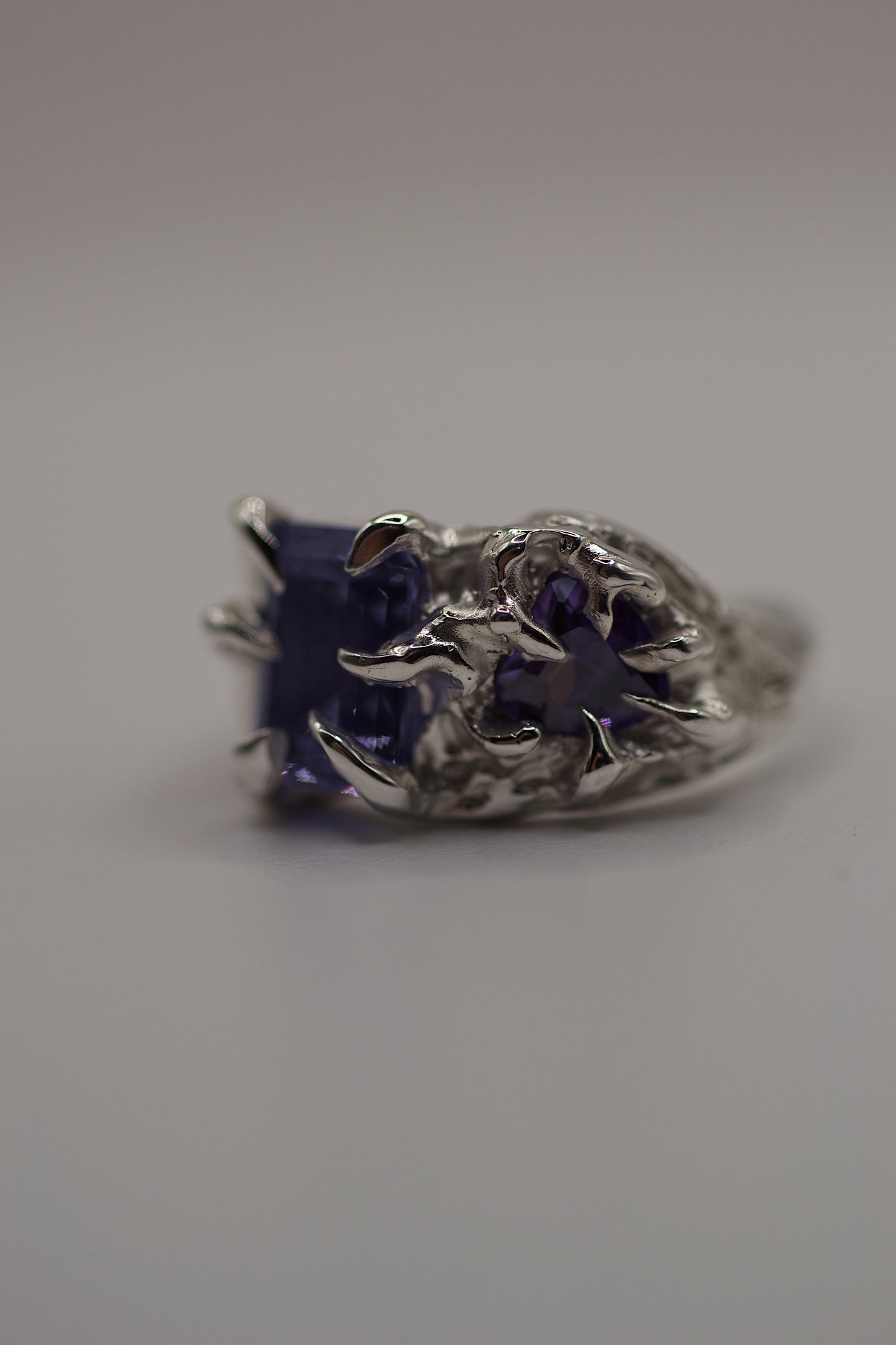 Frontal view of the ring highlighting both purple stones cradled by gothic-style claws. The molten, organic texture of the silver surface indicates its handmade origin via the lost wax casting method.