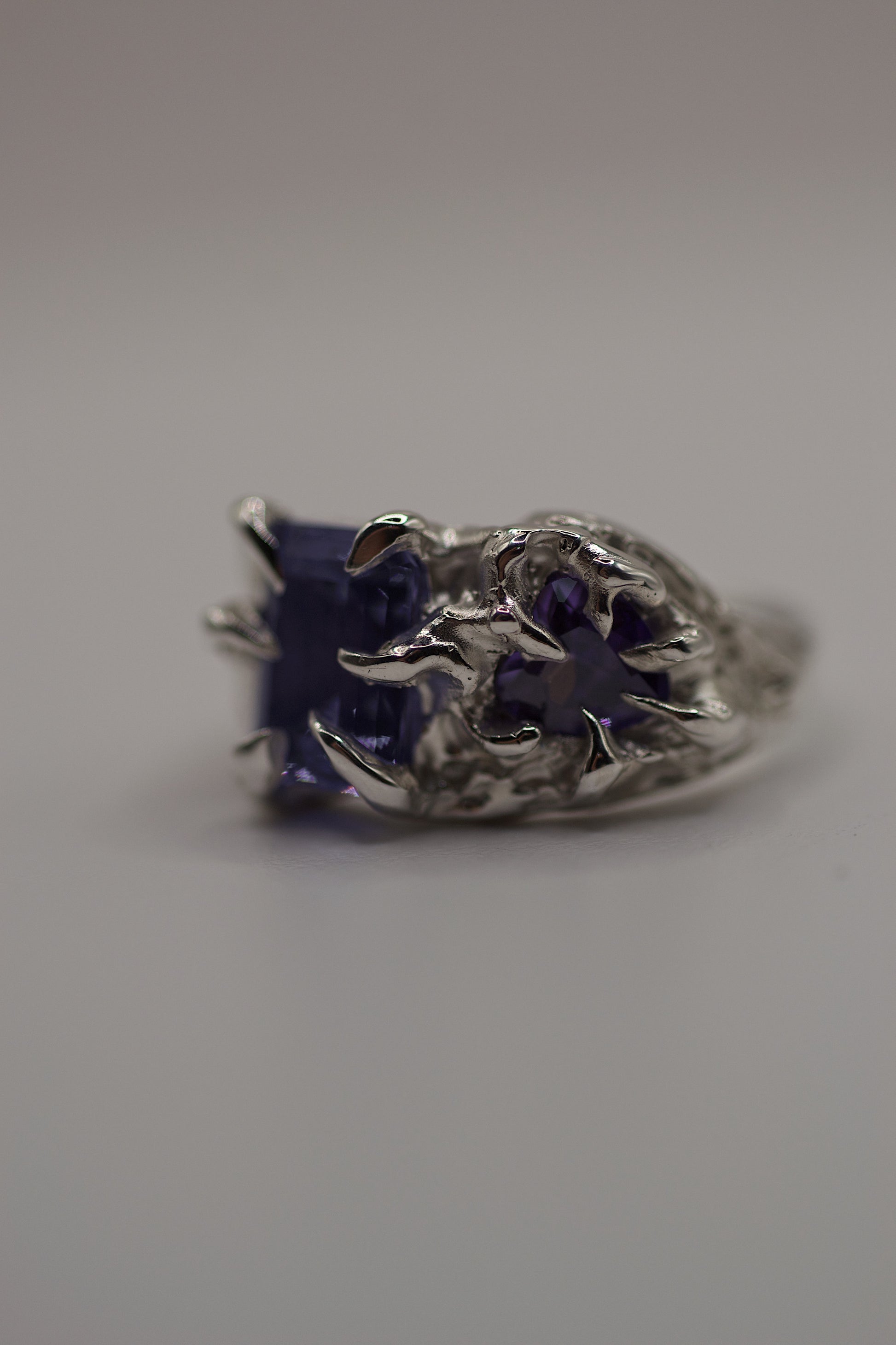Frontal view of the ring highlighting both purple stones cradled by gothic-style claws. The molten, organic texture of the silver surface indicates its handmade origin via the lost wax casting method.