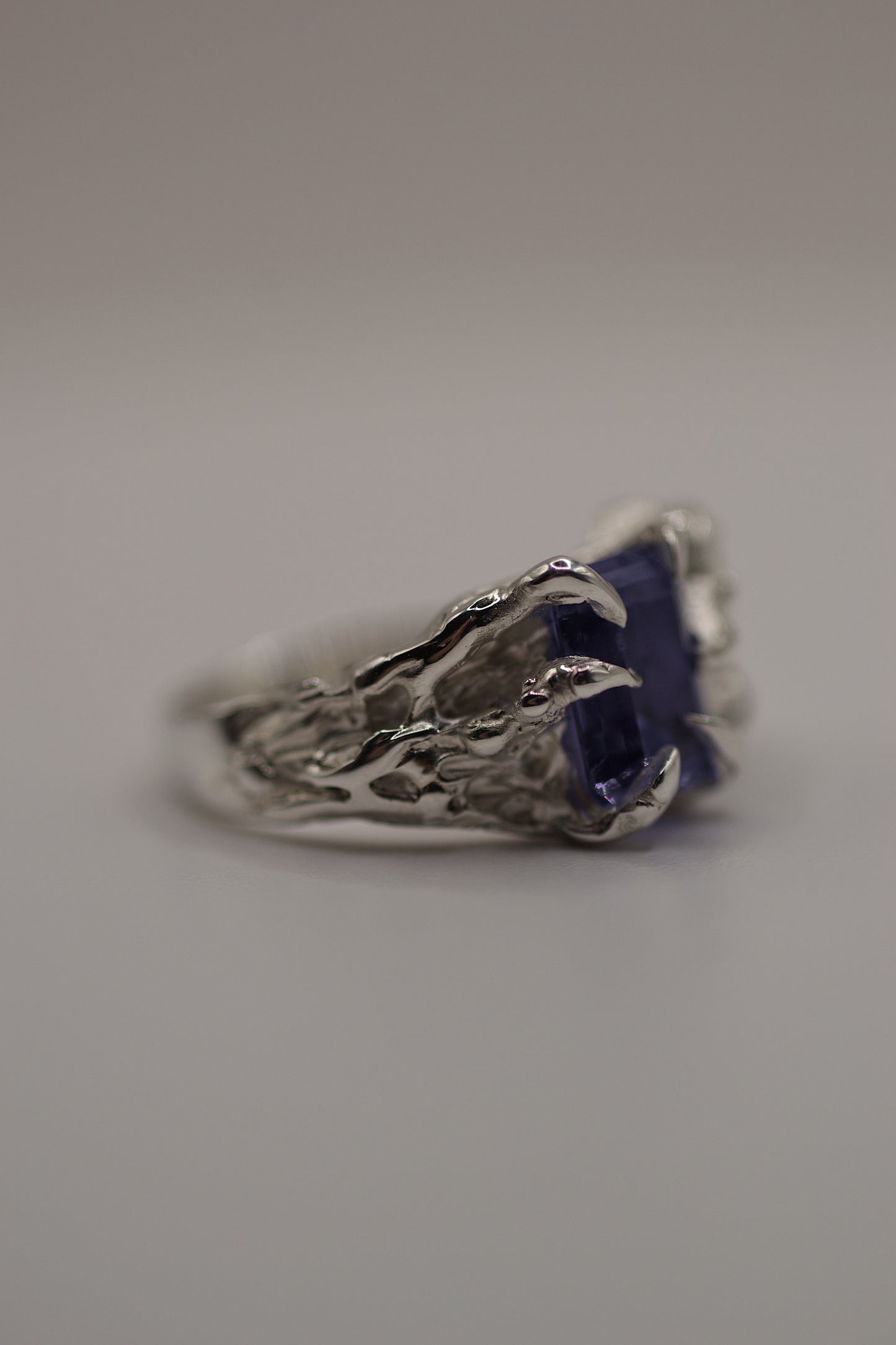 Profile shot of the ring resting on a flat surface, showing the curved claws and detailed molten texture. The gothic setting and handcrafted finish reflect the lost wax casting process.