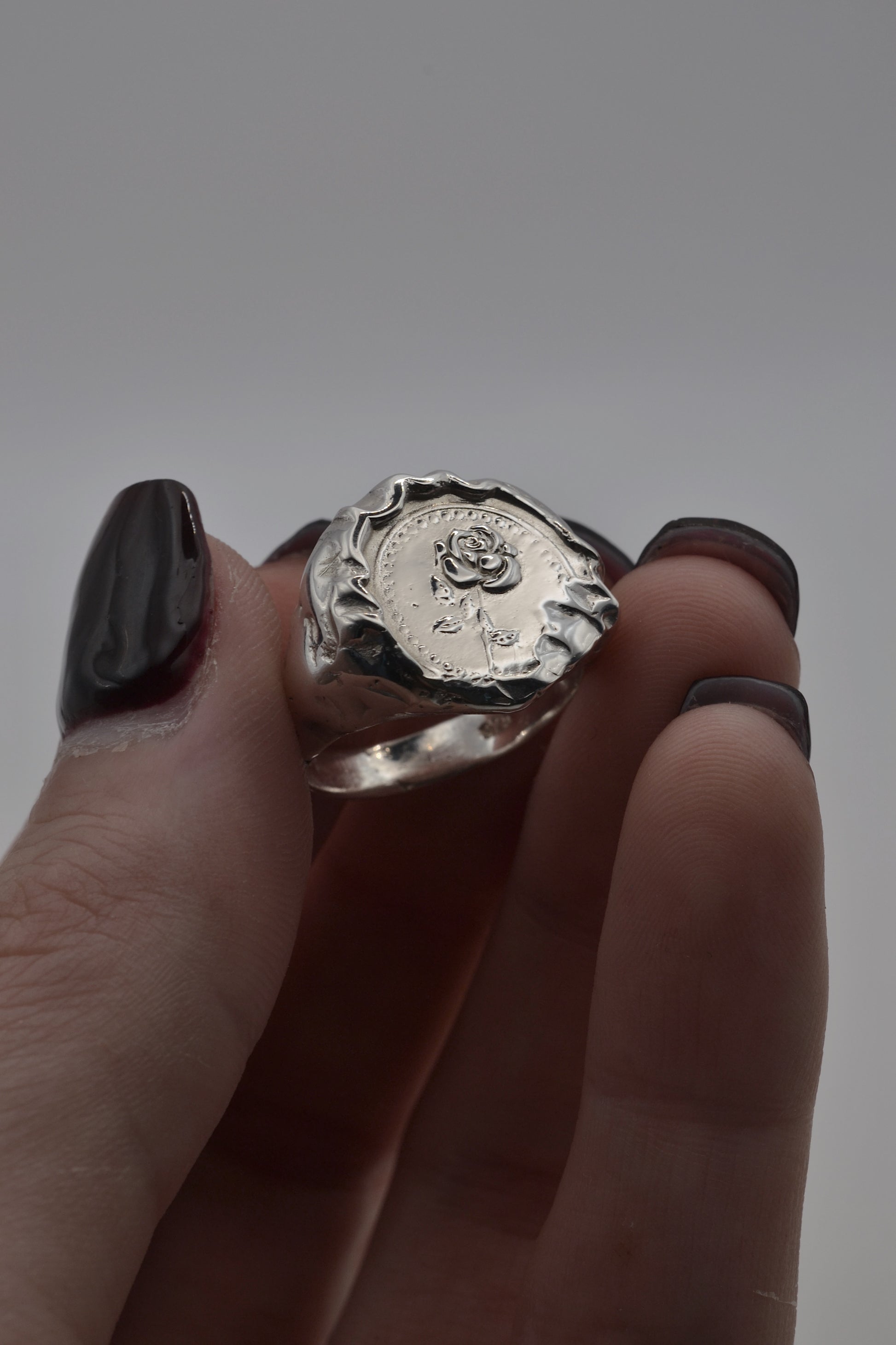 Hand-sculpted lost wax silver ring with embossed rose detail and raw molten texture edges, showcasing an organic handmade finish.