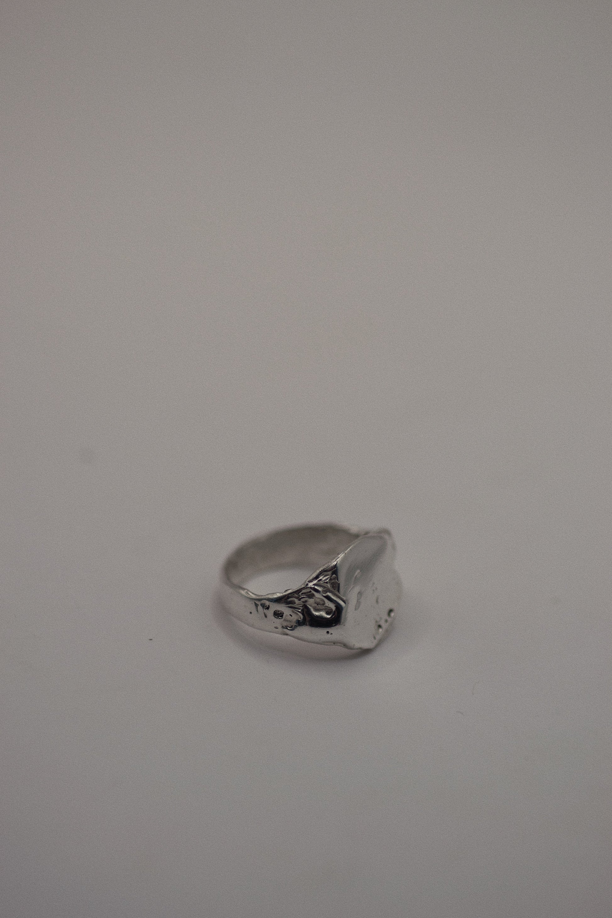 This 925 sterling silver signet ring is sculpted with organic dips and grooves that add dimension and texture to the flat surface. The smooth, sleek band complements the rugged finish, where dips and subtle craters are designed to evoke a natural, earthy look. Made using the lost wax method, this ring showcases the beauty of handcrafted silver, with each piece carrying its own unique texture and character.