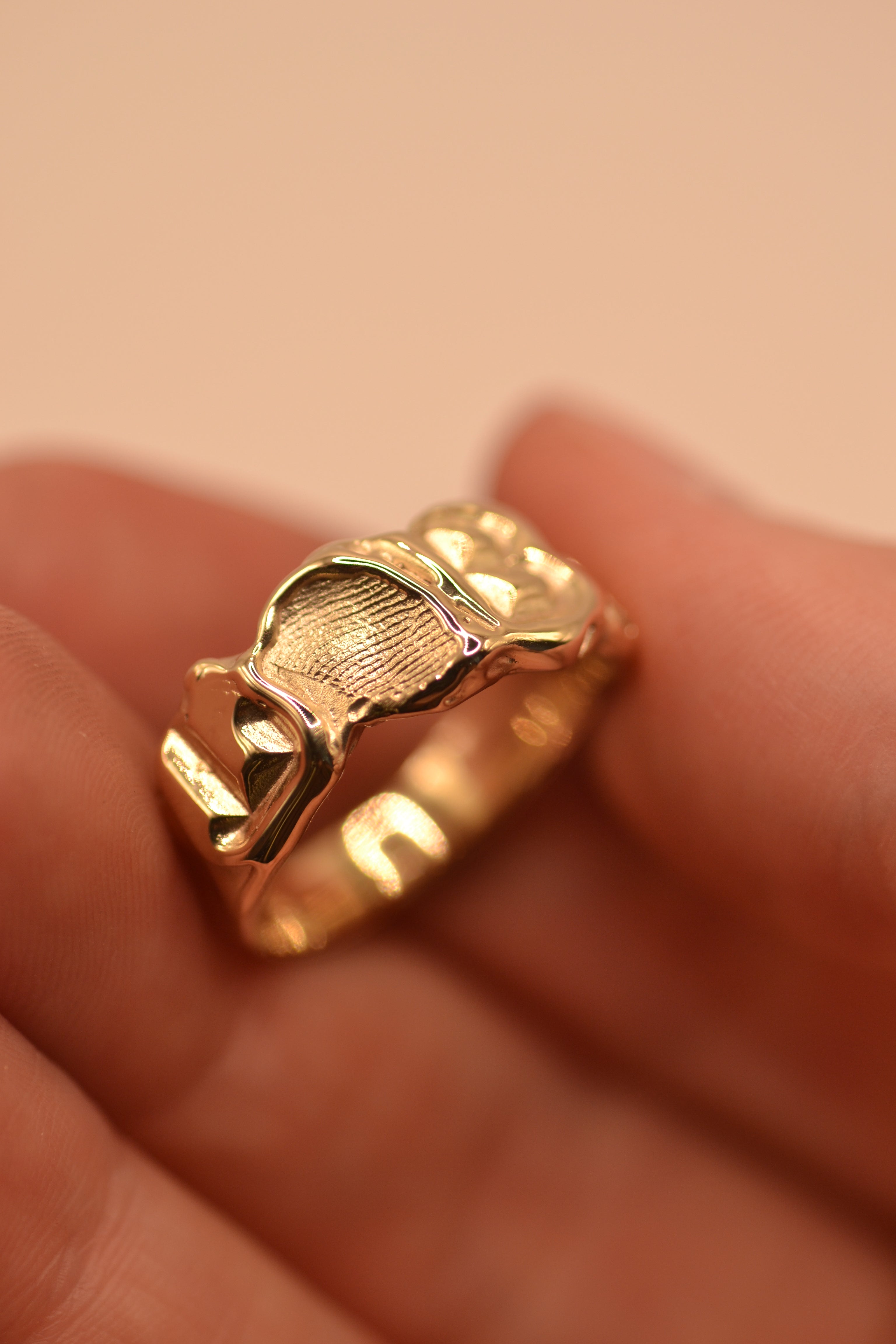 Gold personalised initial band held between fingers showing sculptural lost wax cast texture