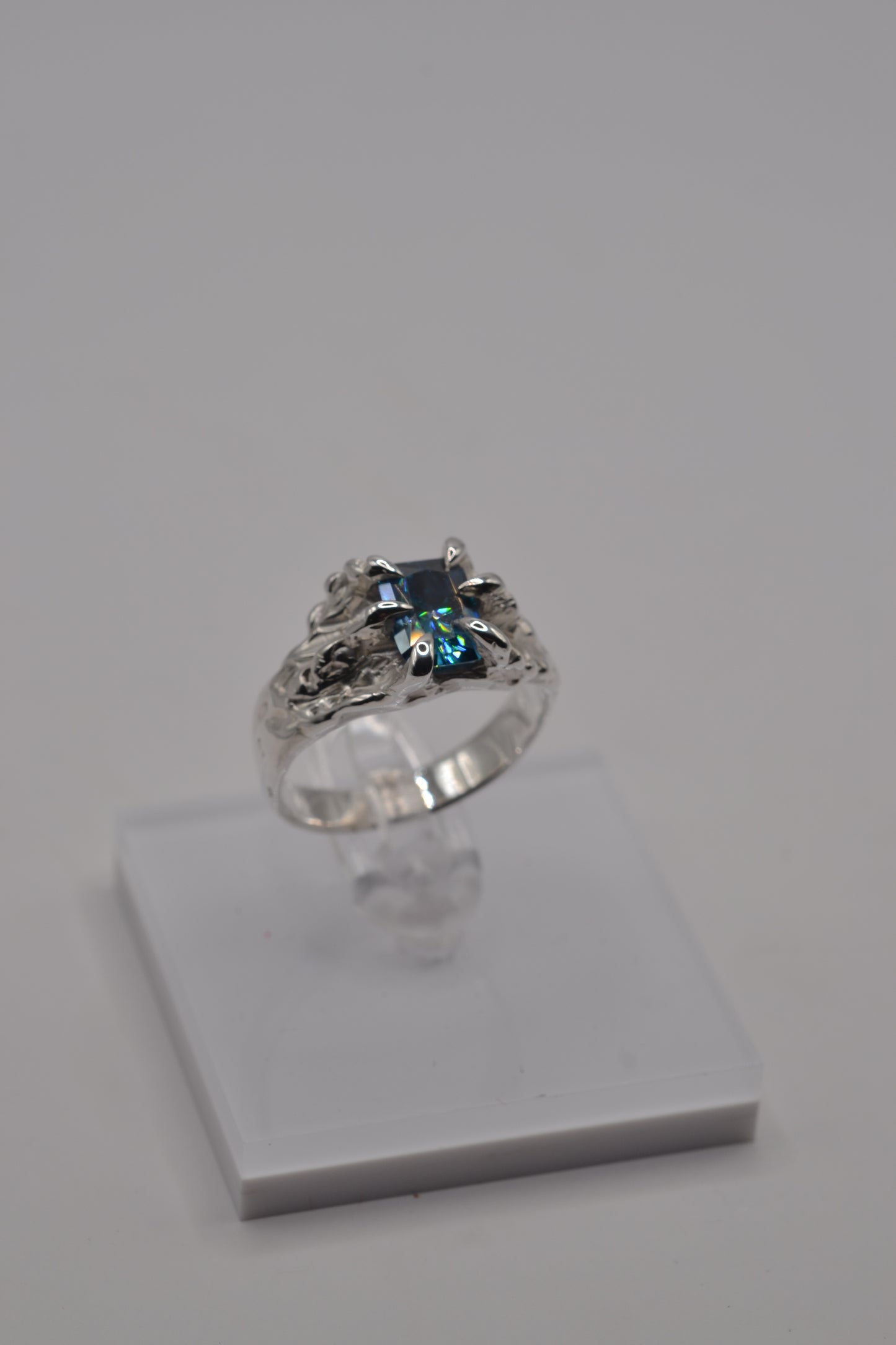 Alternative silver ring displayed on stand, handcrafted using the lost wax technique and set with a blue radiant cut moissanite.