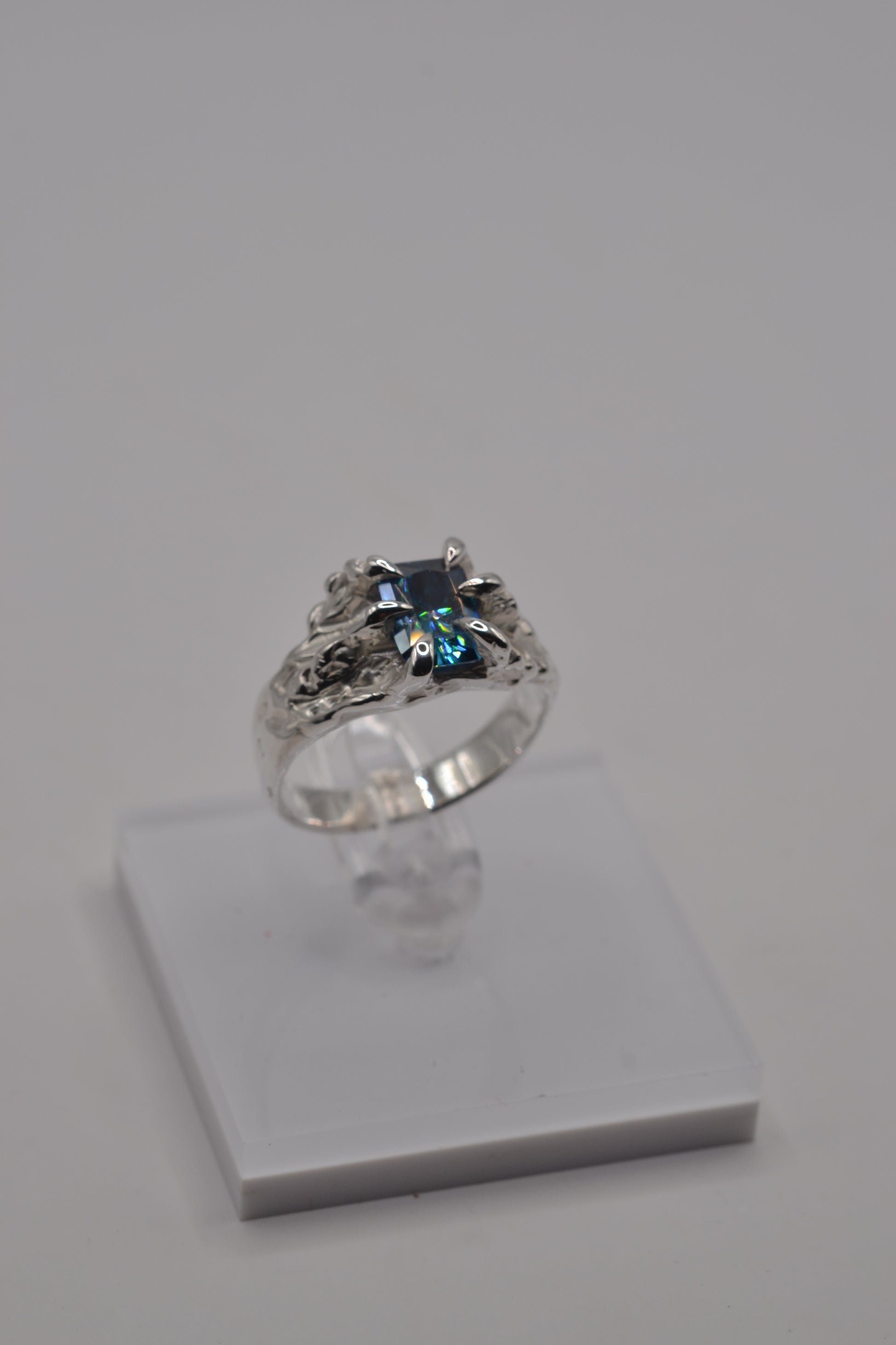 Alternative silver ring displayed on stand, handcrafted using the lost wax technique and set with a blue radiant cut moissanite.