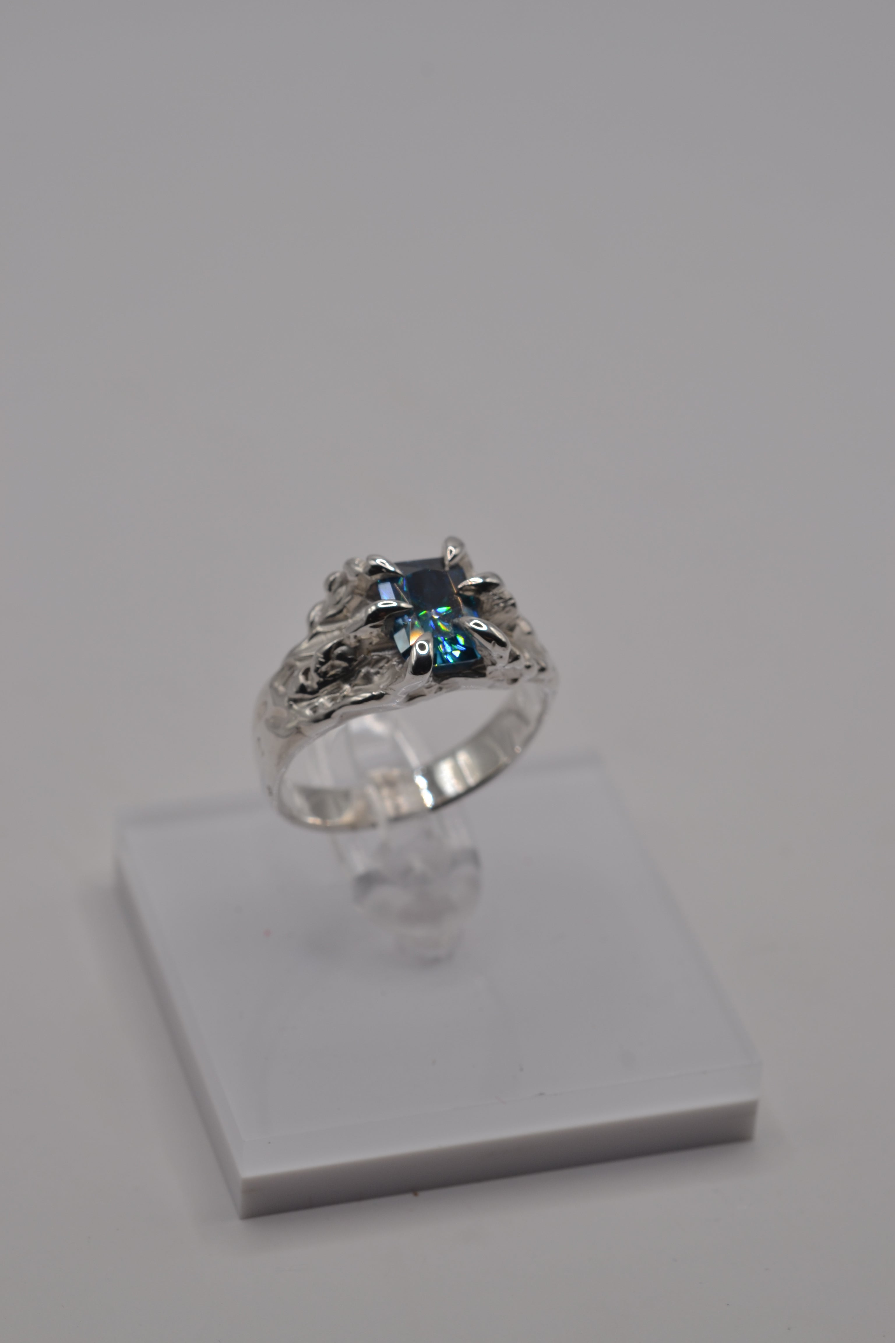 Alternative silver ring displayed on stand, handcrafted using the lost wax technique and set with a blue radiant cut moissanite.