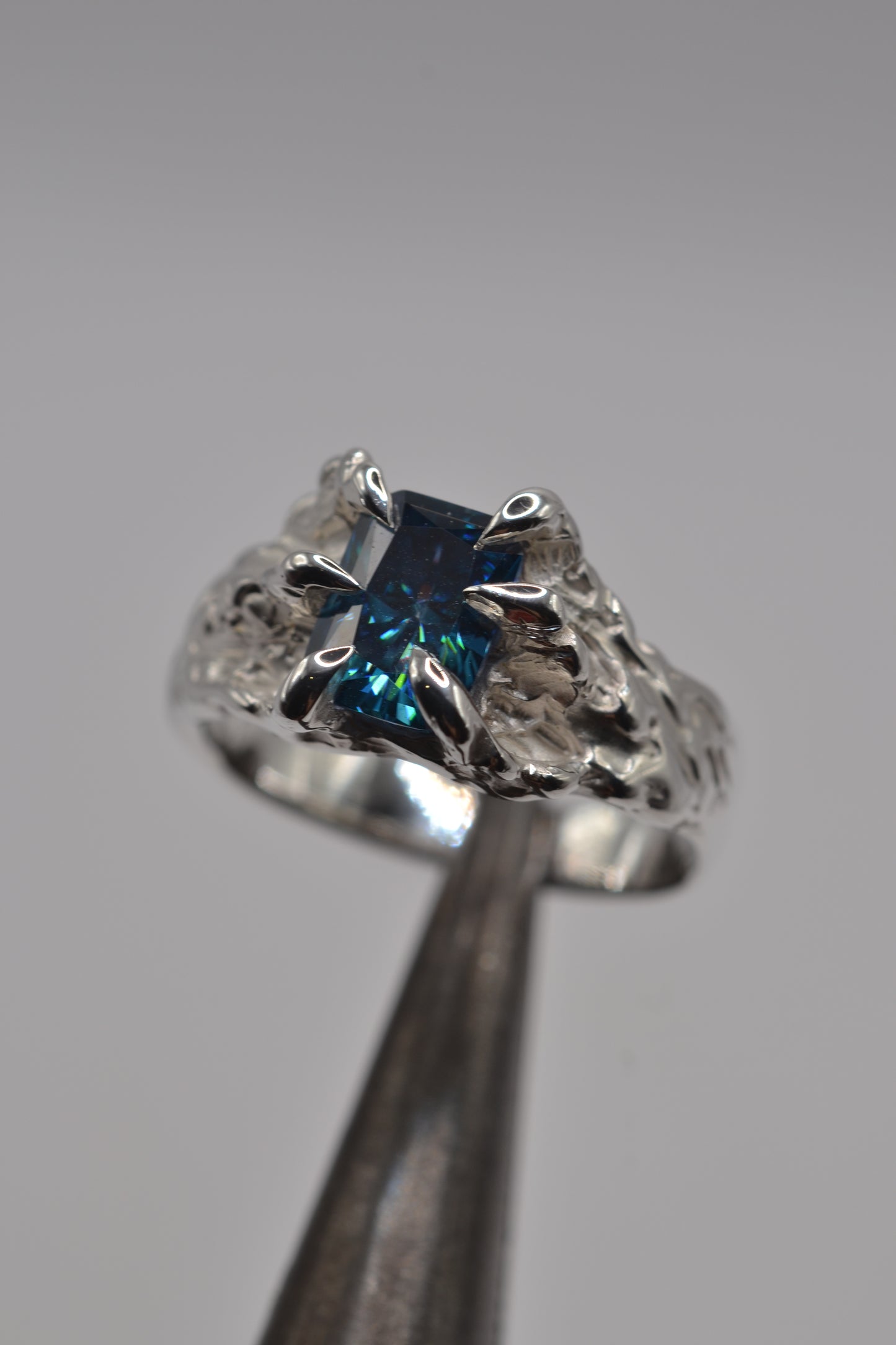 Handmade lost wax silver ring with a blue radiant cut moissanite, showcasing an alternative molten metal design.