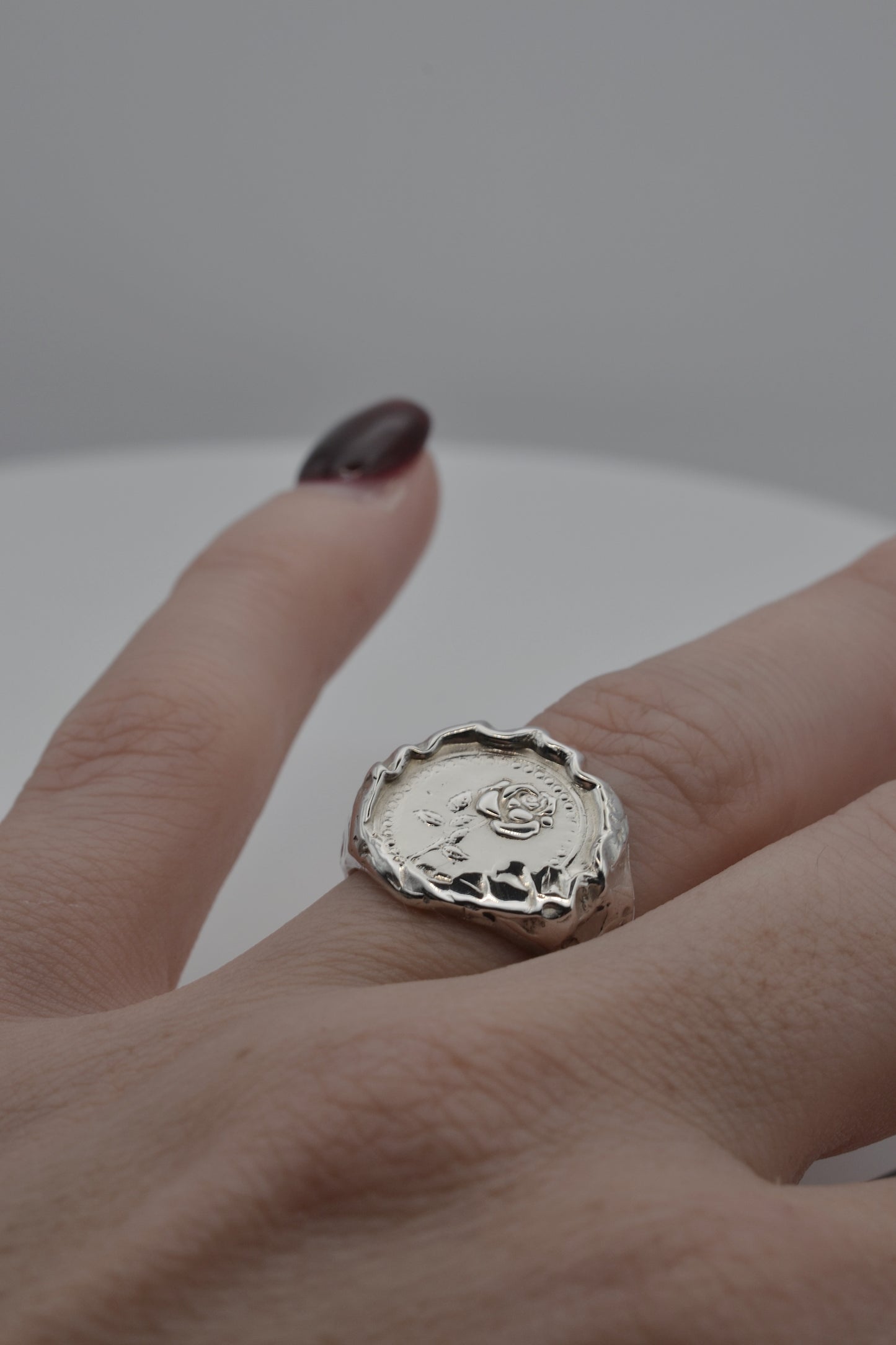 Handmade molten silver signet ring worn on the hand, featuring an embossed rose and organic gothic texture created using the lost wax technique.