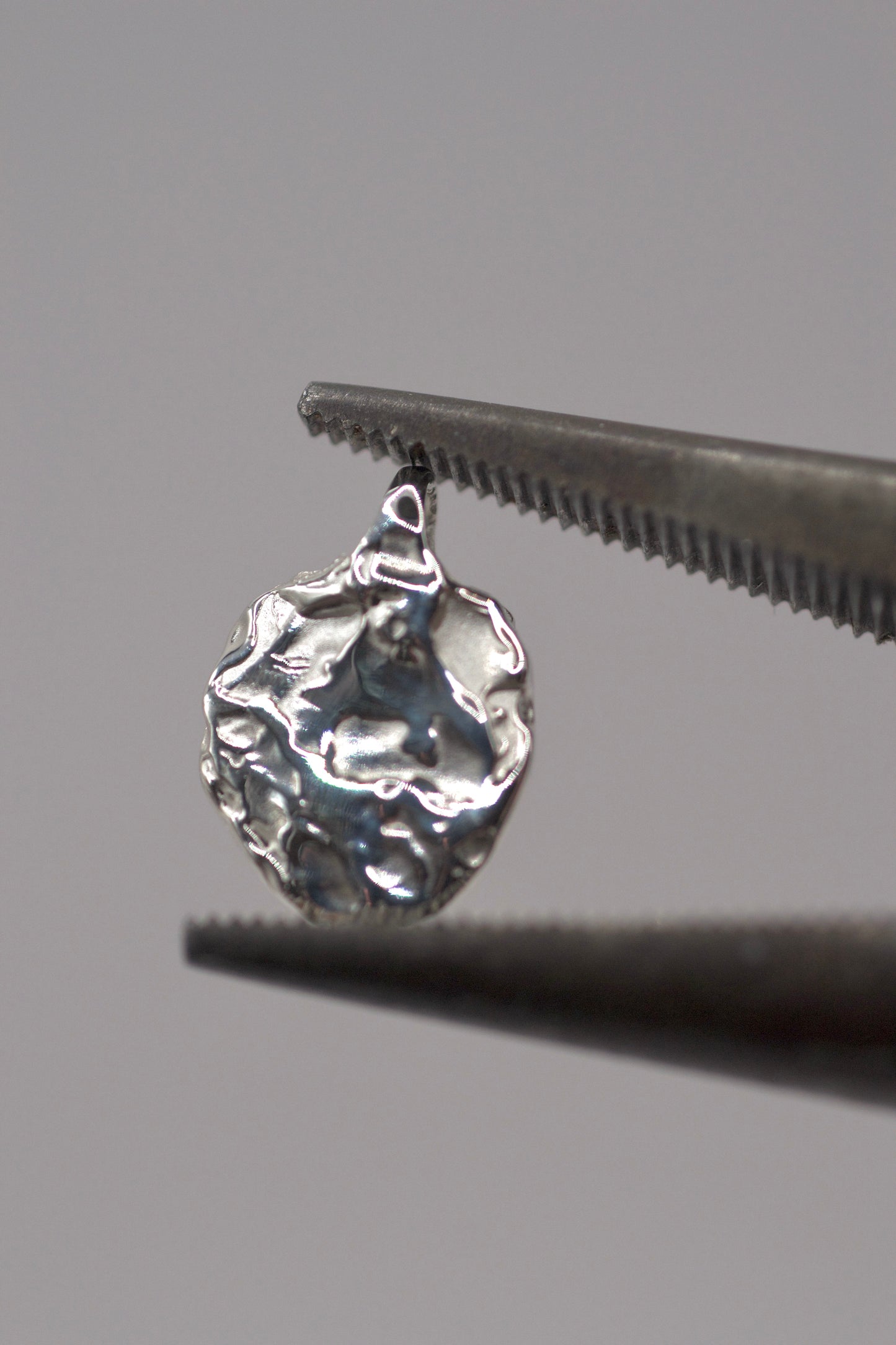 Close-up of handcrafted 925 sterling silver molten pendant made with the lost wax casting technique, shown held in jewellery pliers.