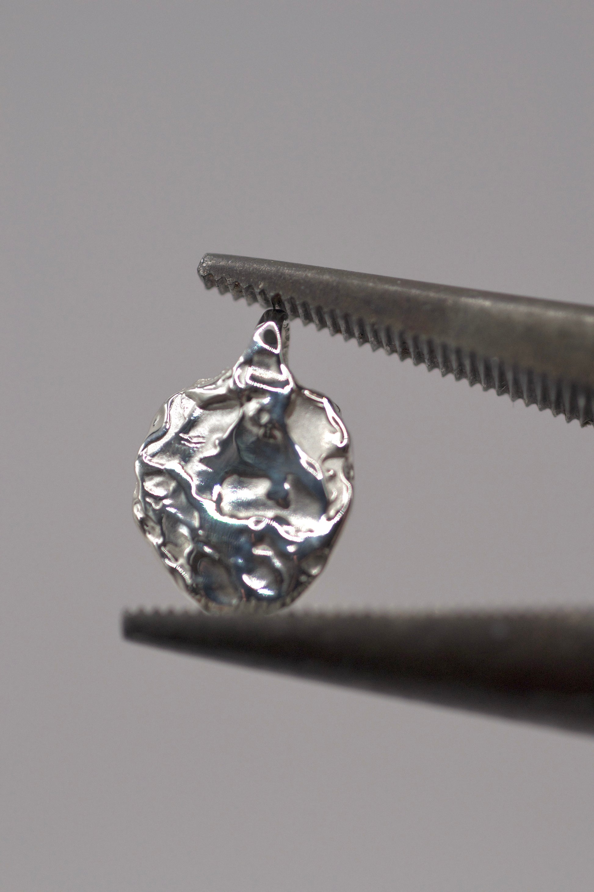 Close-up of handcrafted 925 sterling silver molten pendant made with the lost wax casting technique, shown held in jewellery pliers.