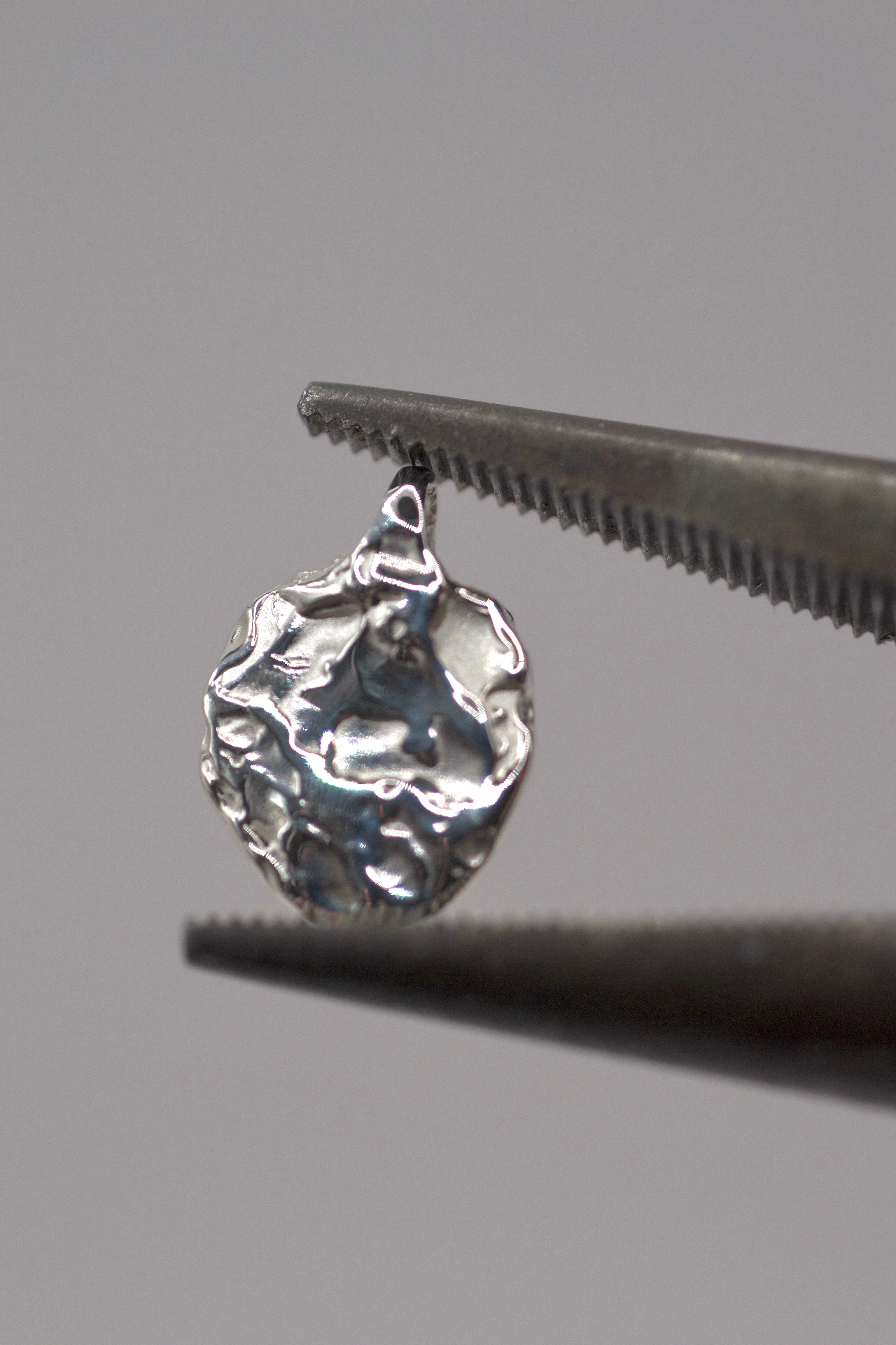 Close-up of handcrafted 925 sterling silver molten pendant made with the lost wax casting technique, shown held in jewellery pliers.