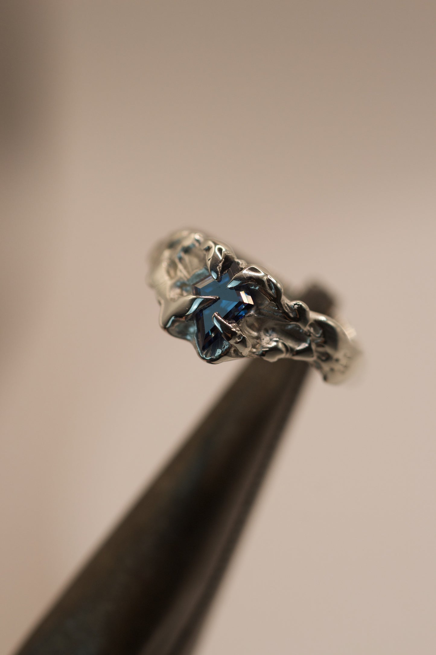 his asymmetrical lost wax ring in 925 sterling silver has an organic molten texture with gothic inspired claws gripping a vivid blue kite cut moissanite, designed for alternative fashion or engagement.
