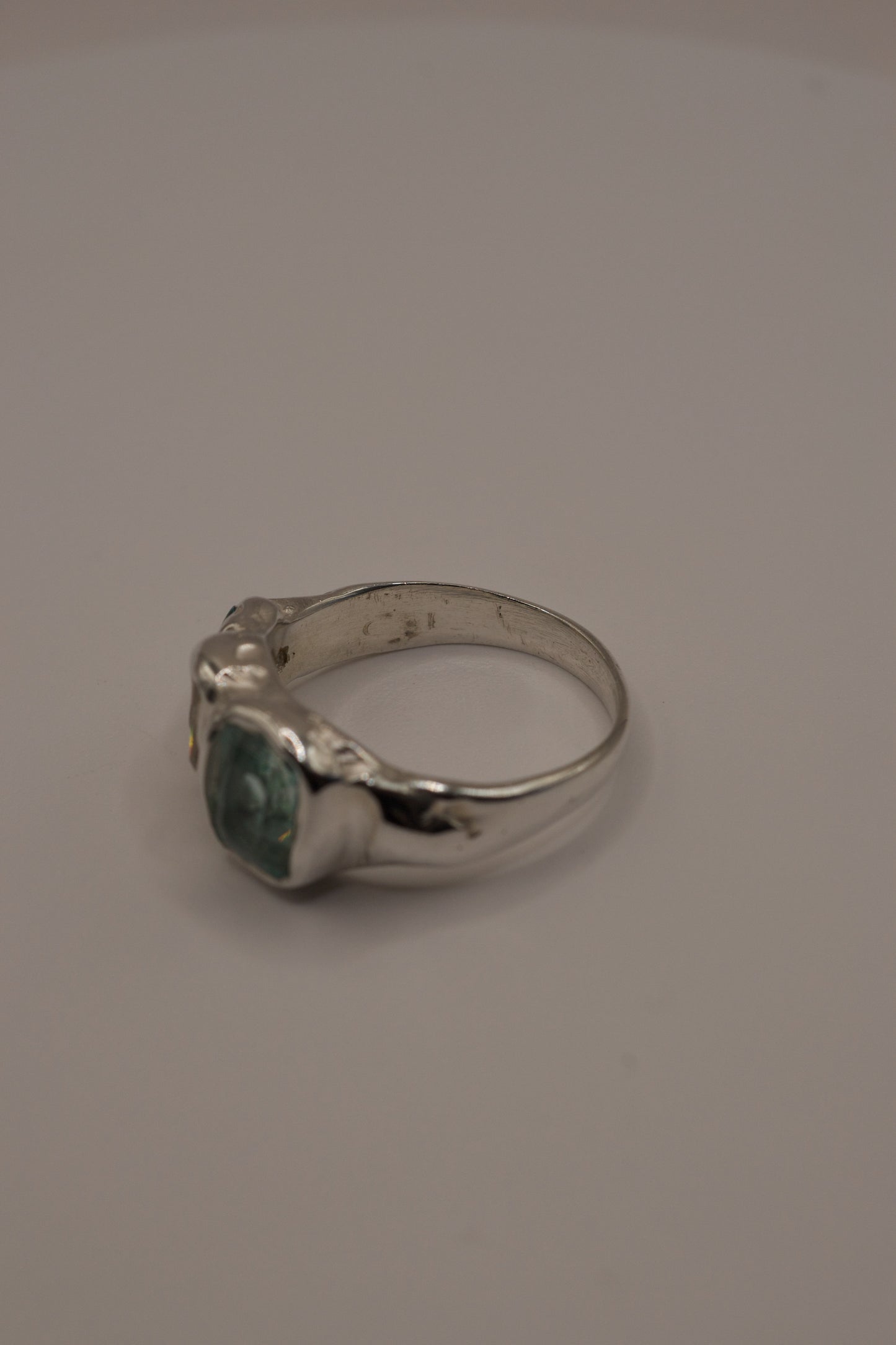 Profile view of an organic silver ring with flowing molten texture, high polish band, and three gemstones cast in place: a central seafoam green crystal, baguette-cut moissanite, and small green crystal, crafted using the lost wax jewellery making process.