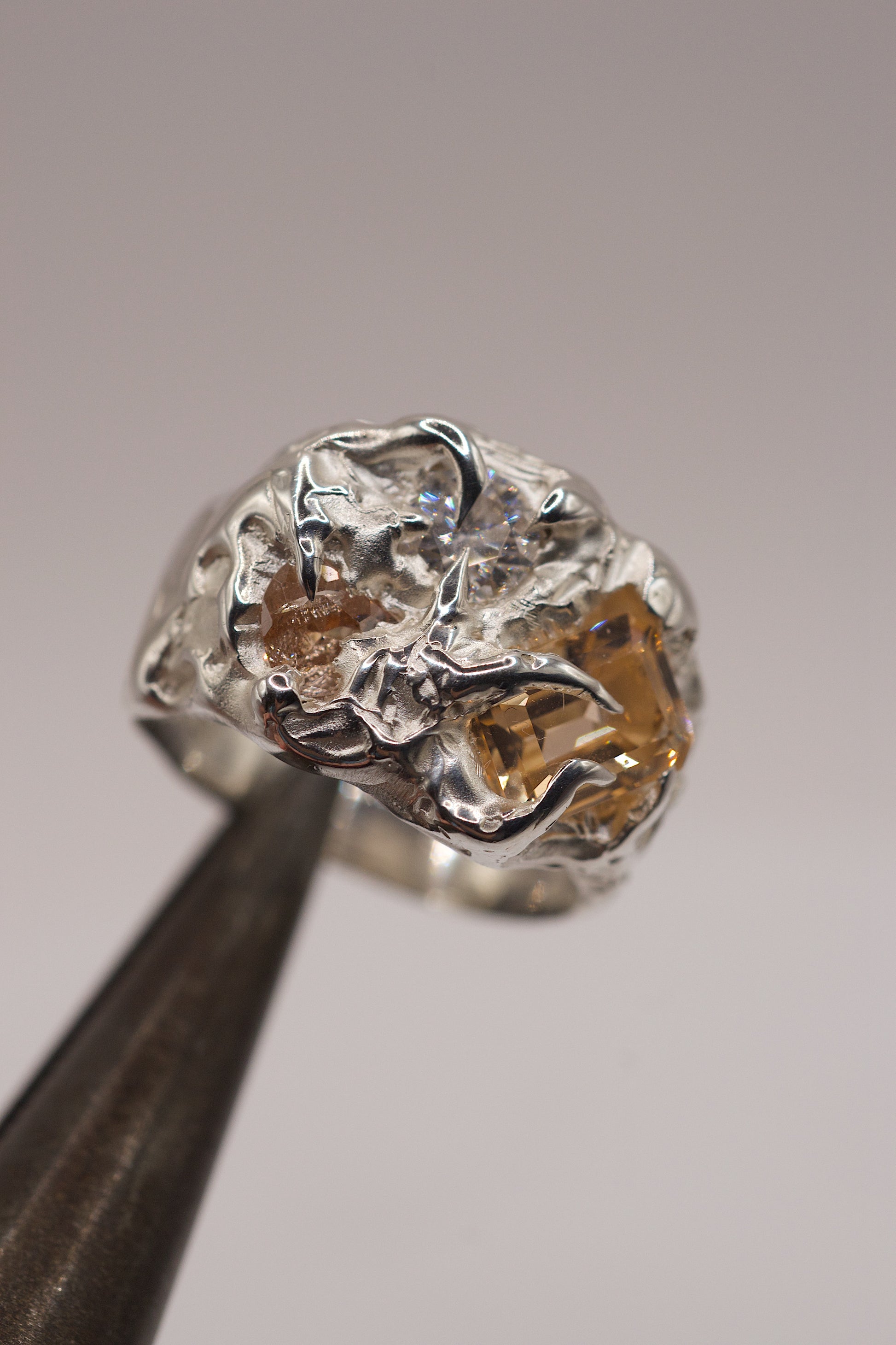 Molten silver ring with heavy texture and citrine gemstones on a grey background.