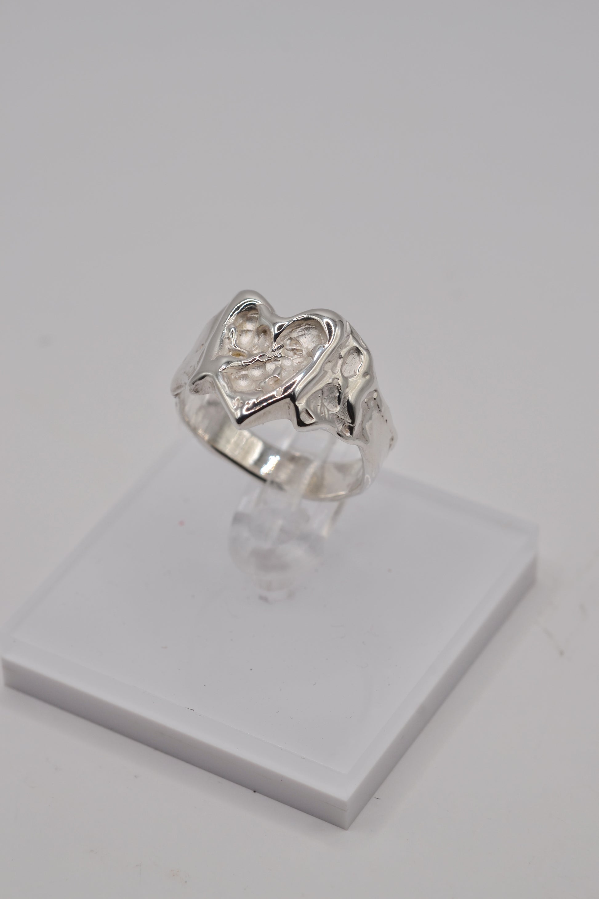 Organic lost wax cast ring displayed on clear stand, sterling silver handmade heart ring from side angle