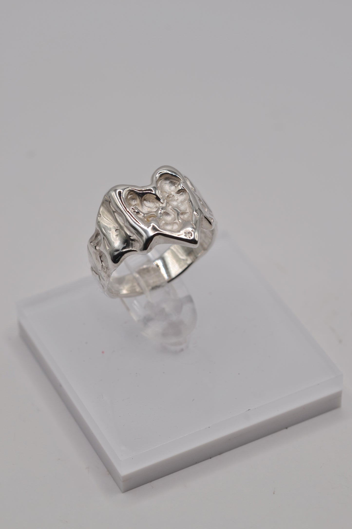 Organic lost wax cast ring displayed on clear stand, sterling silver handmade heart ring from side angle left view