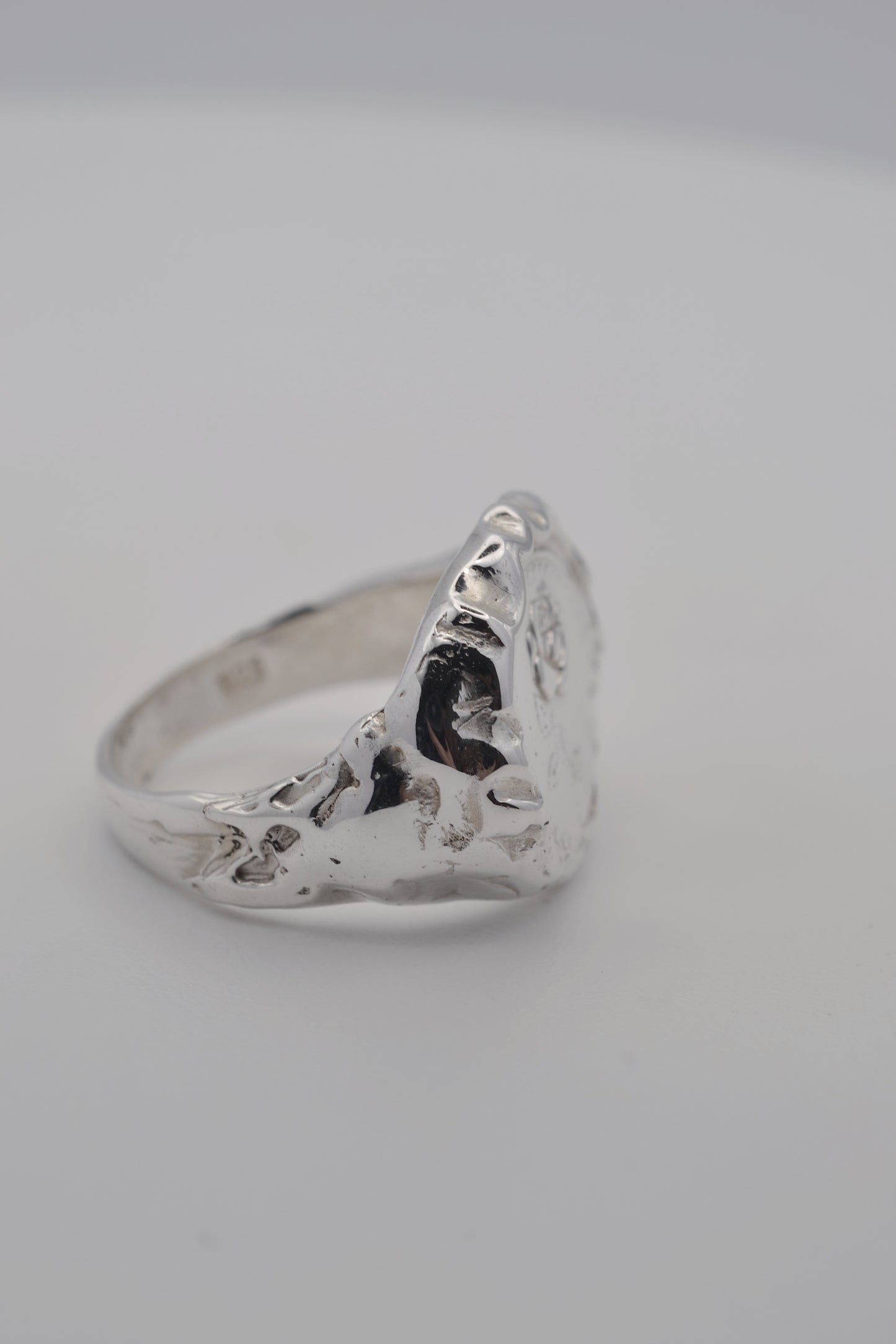 Handmade lost wax silver ring with sculptural molten edges and a raised embossed rose design, photographed during finishing.