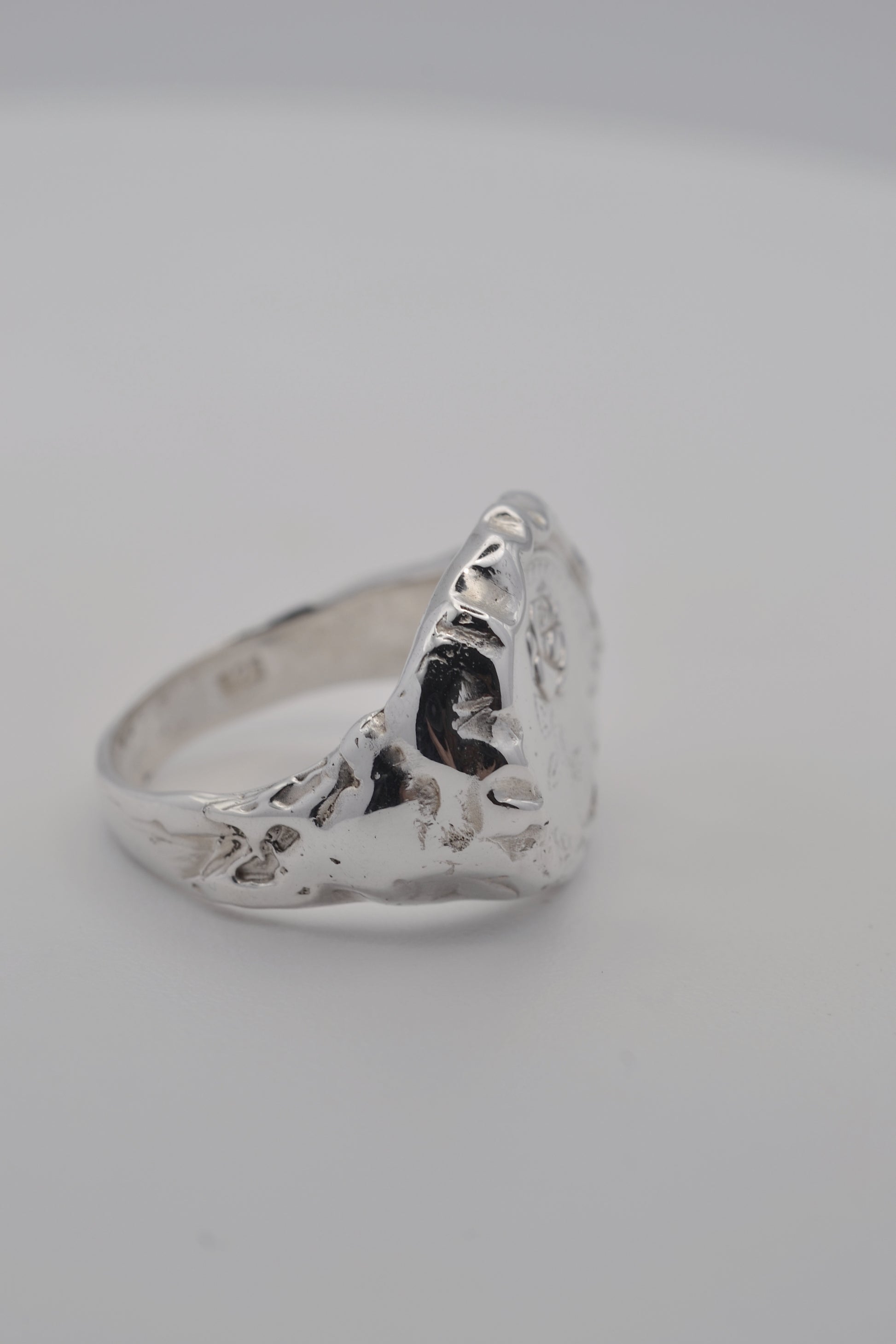 Handmade lost wax silver ring with sculptural molten edges and a raised embossed rose design, photographed during finishing.