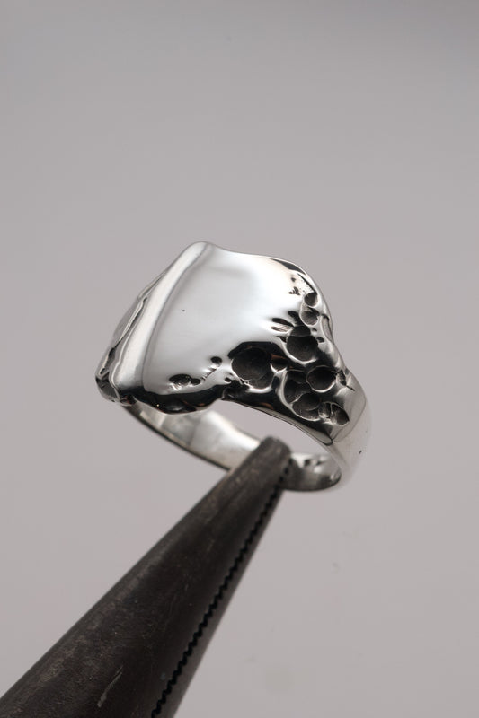 A macro close-up of the handcrafted sterling silver signet ring, showing crater-like molten details and smooth polished surface created using the lost wax technique.