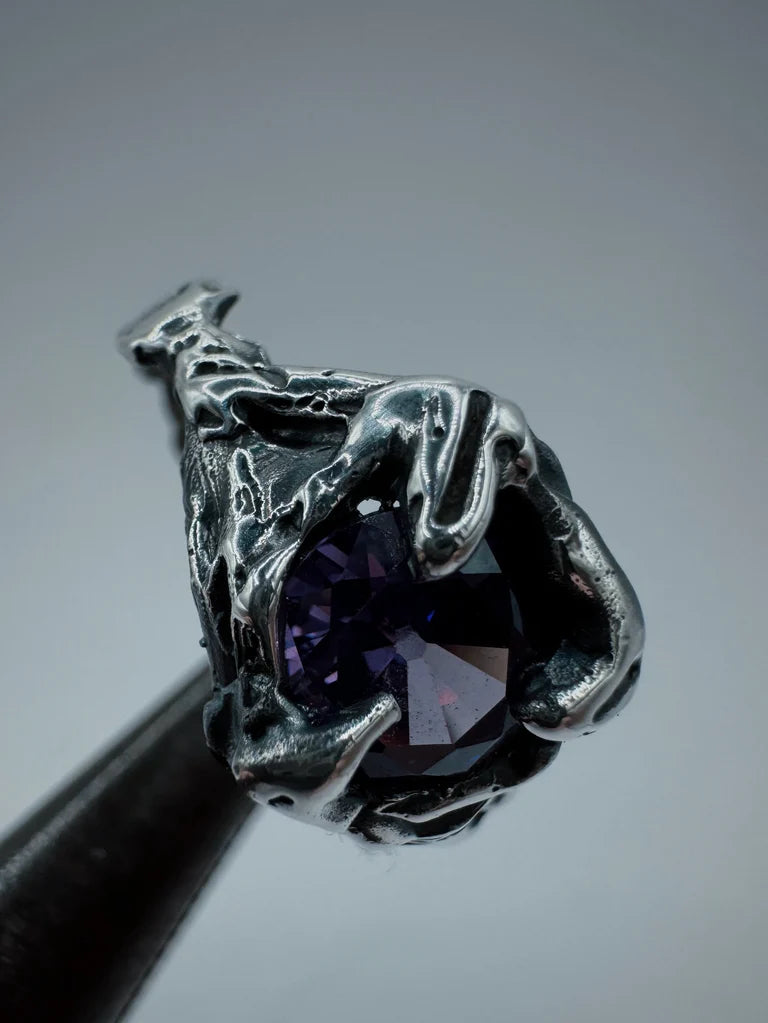 This ring is crafted from molten metal sterling silver, highlighting a beautiful amethyst centerpiece surrounded by three gothic claw settings. The detailed grooves and blackened dimension enhance its allure, while the organic texture comes from the lost wax technique.