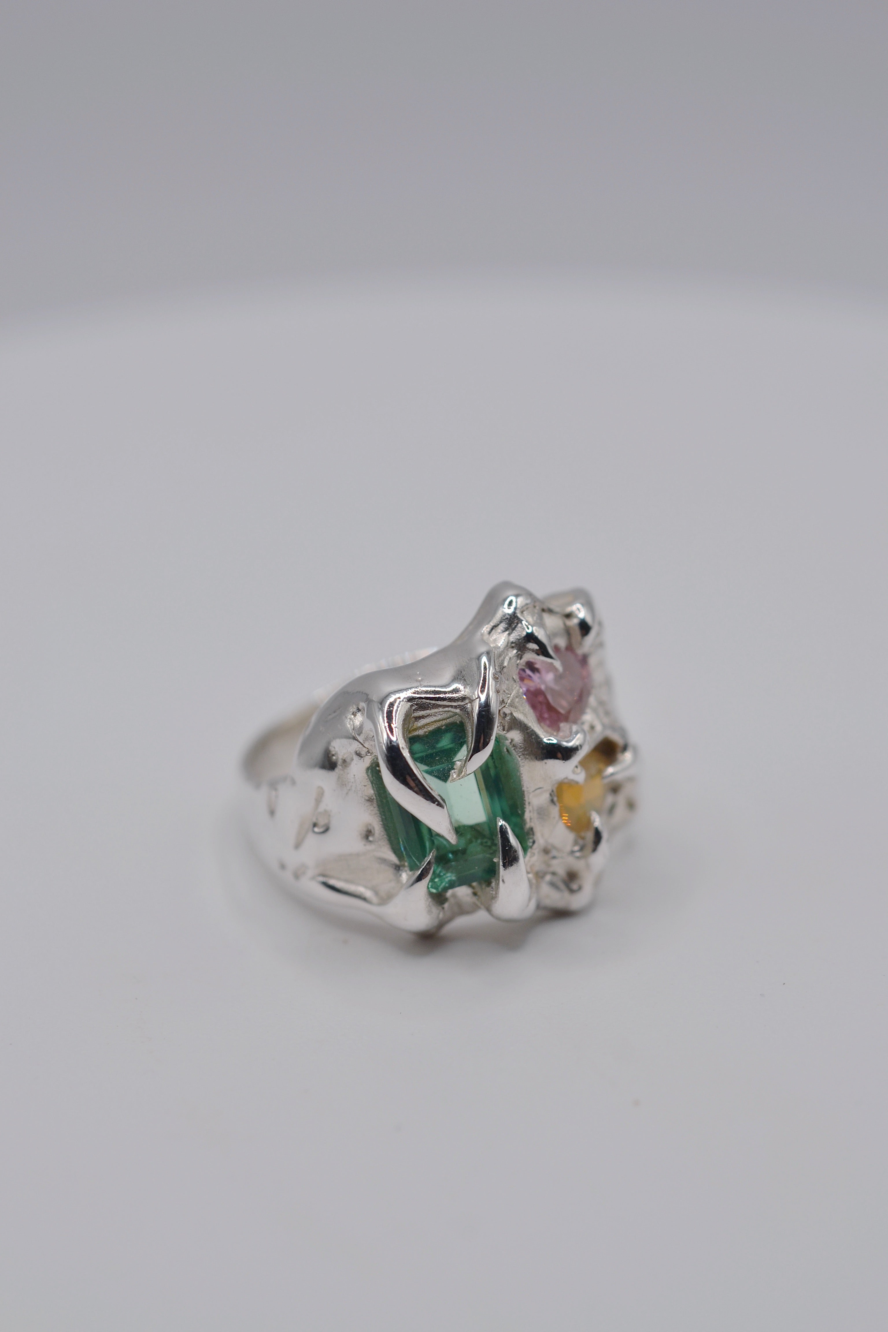 The Mirage ring flat lay. Handmade organic silver, sculpted using wax carving and lost wax casting. Lab-grown green tourmaline, pink heart cubic zirconia and milky yellow opal. Metal Bones Jewellery.