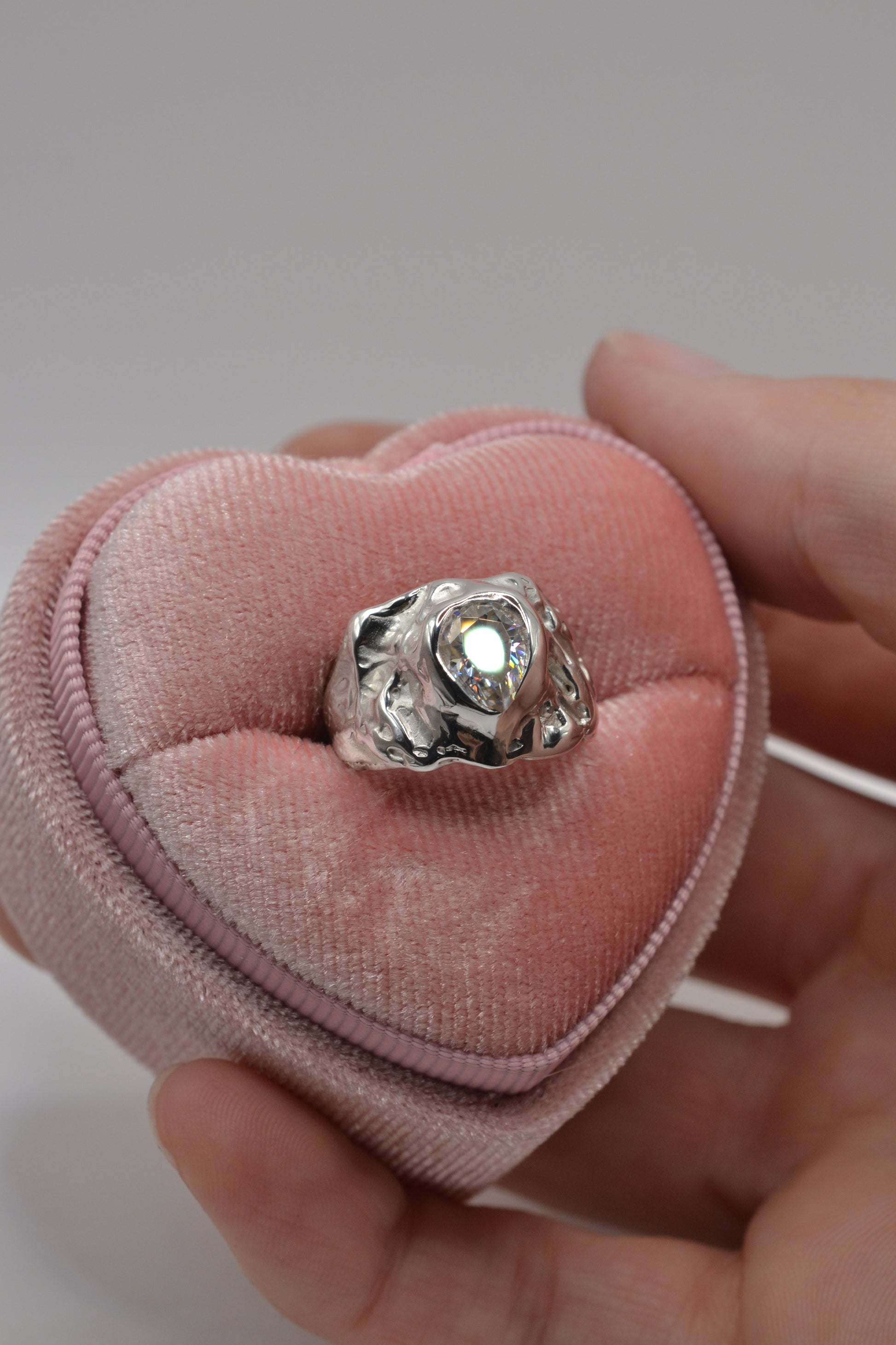 The molten silver lost wax ring presented in a blush pink heart-shaped velvet box, showing its organic, hand-sculpted textures.