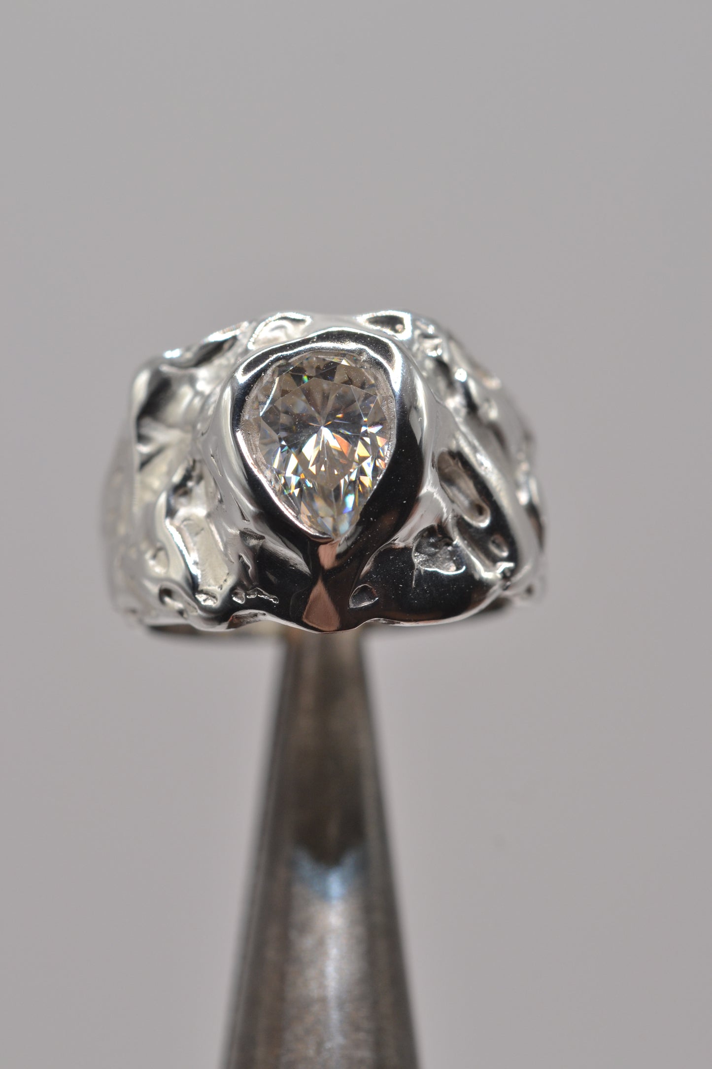 The molten silver moissanite ring displayed on jeweller’s pliers, highlighting the textured lost wax detailing and bold organic shape.