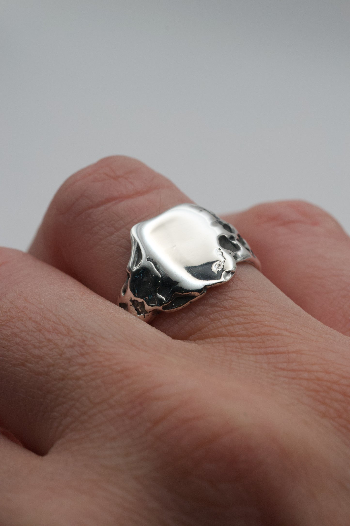 The molten silver signet ring worn on a finger, showing its natural sculpted texture and polished top surface.