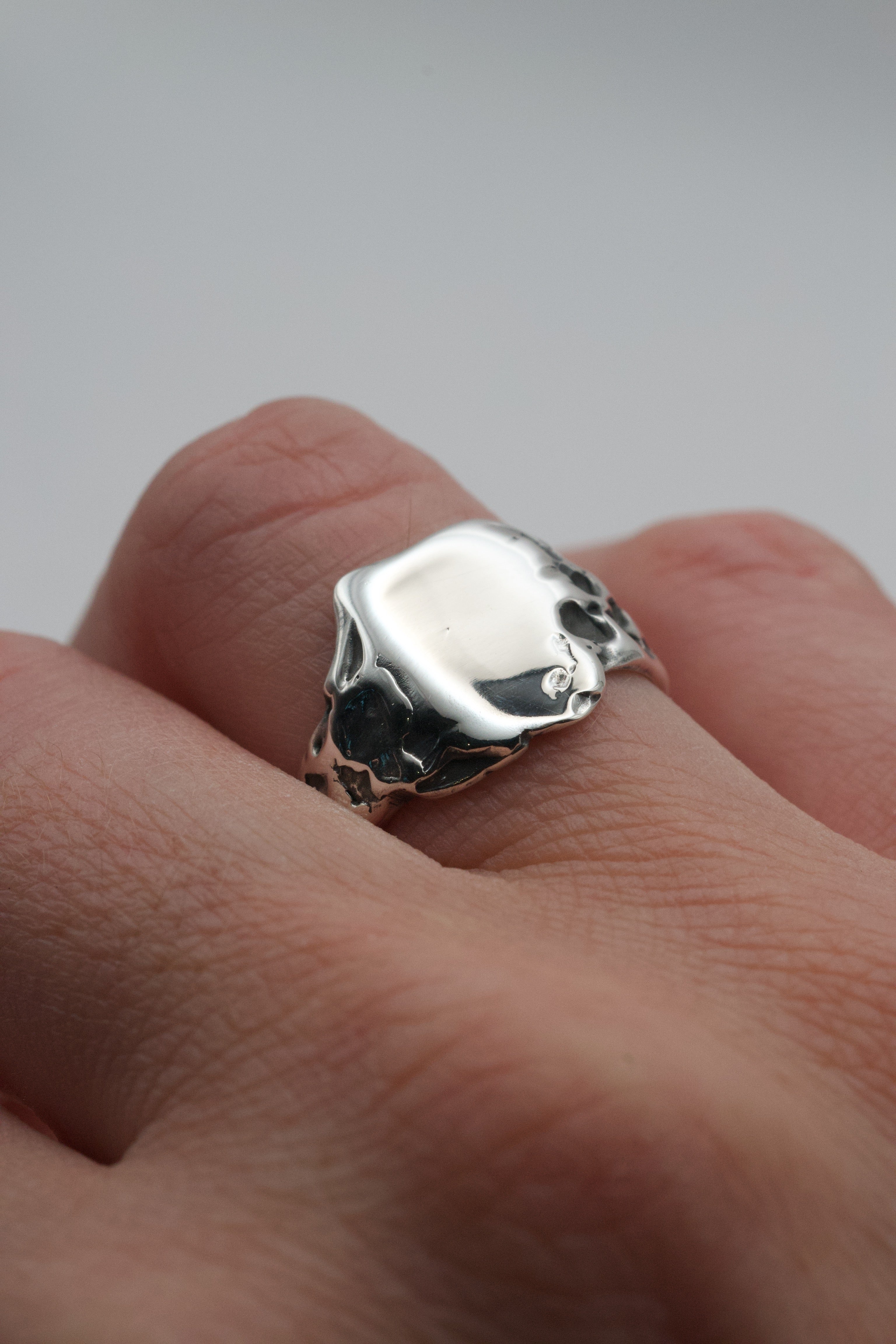 The molten silver signet ring worn on a finger, showing its natural sculpted texture and polished top surface.