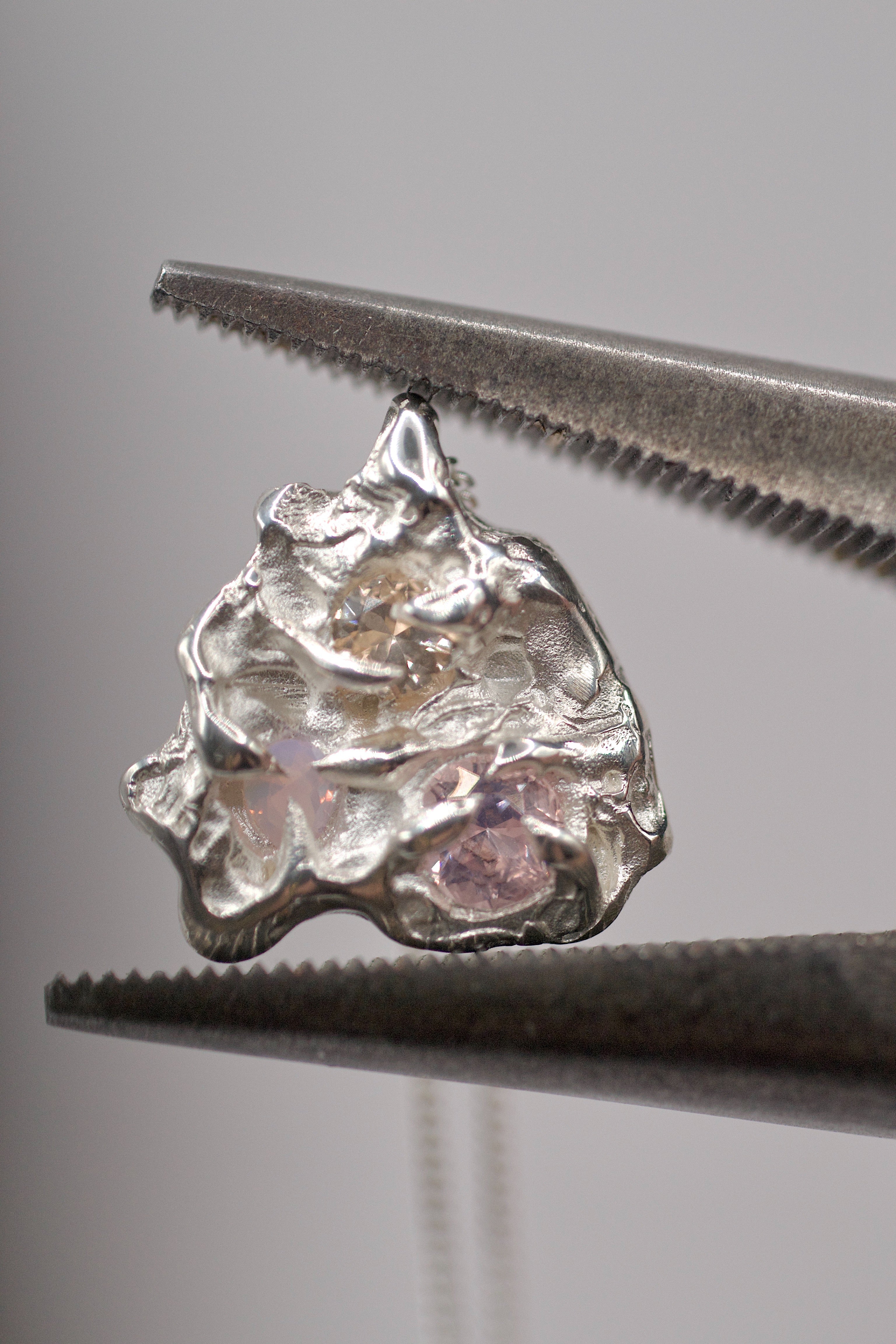 Close-up of a molten textured 925 sterling silver pendant with cast-in-place nano crystals held in jeweller’s tweezers.