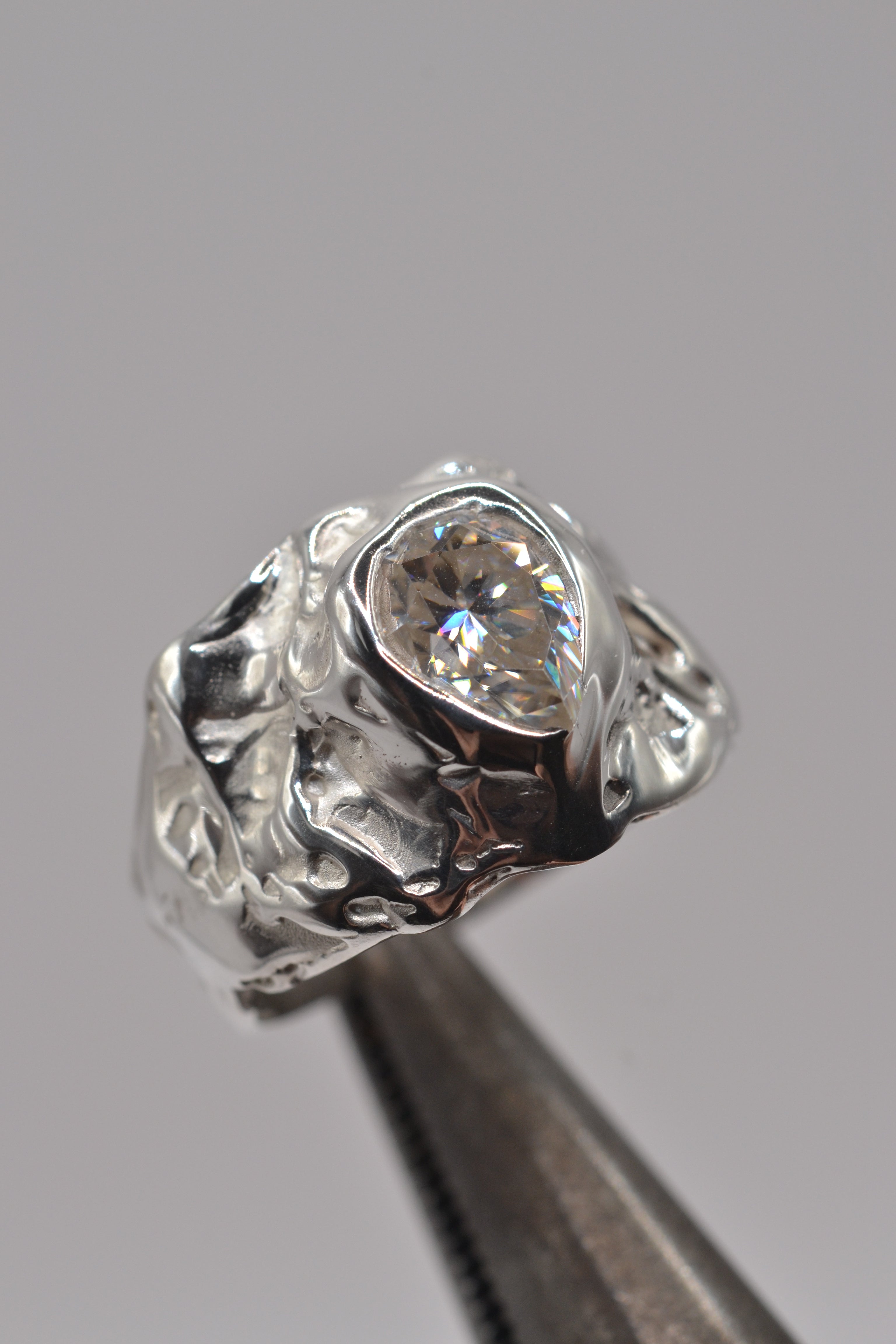 Close-up shot of a handmade molten silver ring featuring a pear-cut moissanite. Sculpted using the lost wax technique, showing organic texture and alternative design.