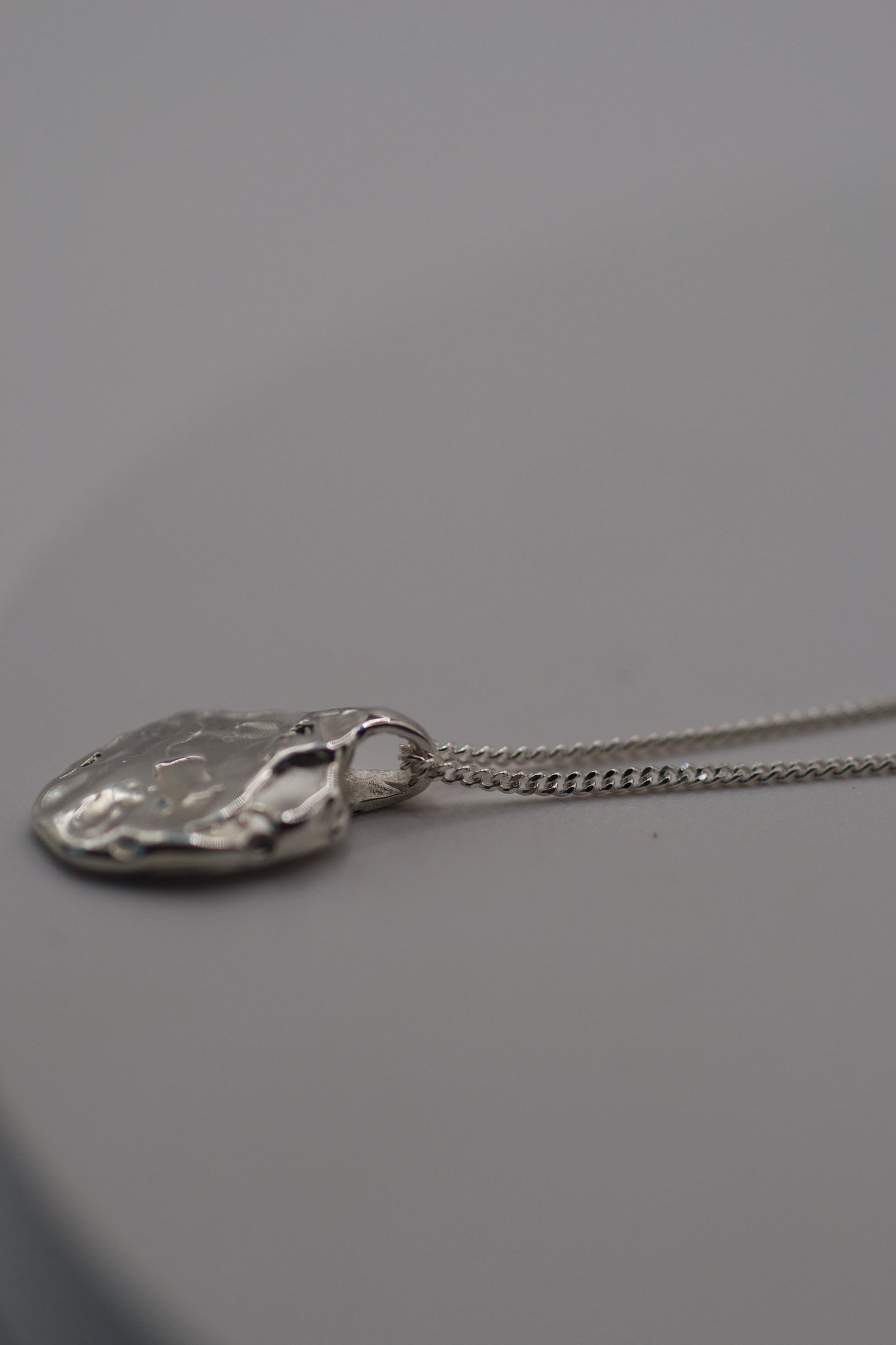 Detailed photo of an artisan-made molten silver pendant and fine sterling silver curb chain, crafted using the lost wax process.