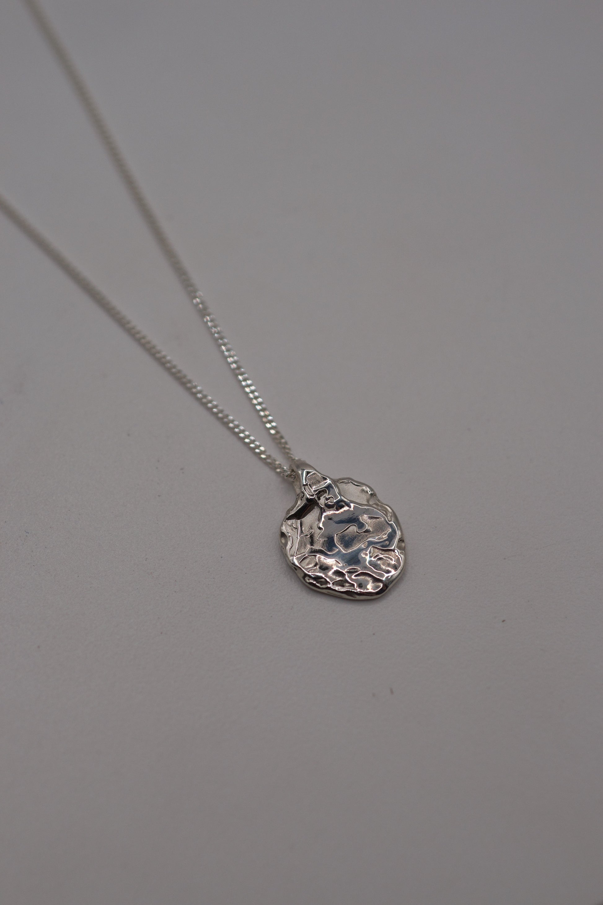 Flat lay photo of a handcrafted molten sterling silver pendant on a delicate chain, featuring organic lost wax textures.