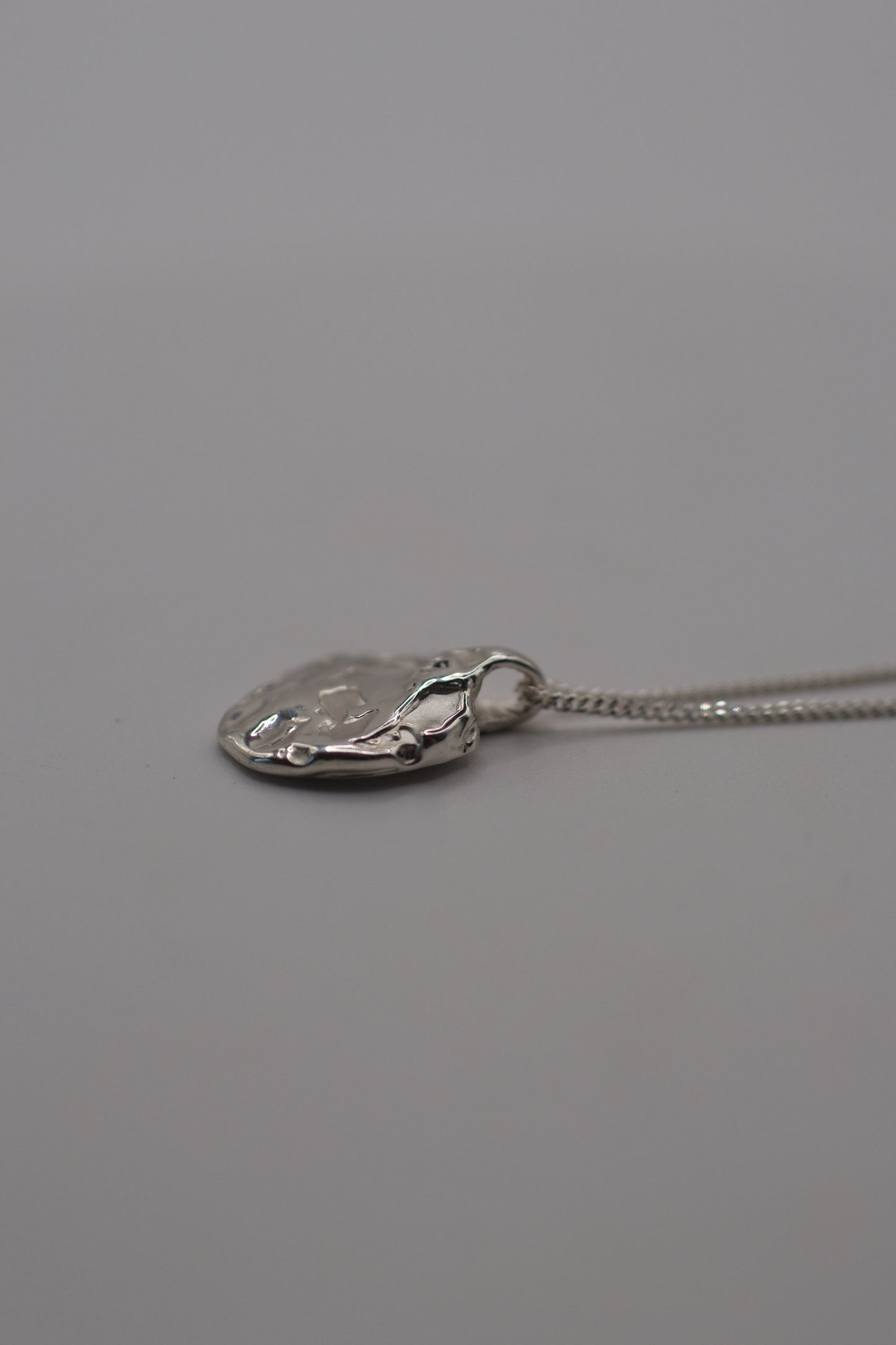 Flat lay photo of a handcrafted molten sterling silver pendant on a delicate chain, featuring organic lost wax textures.