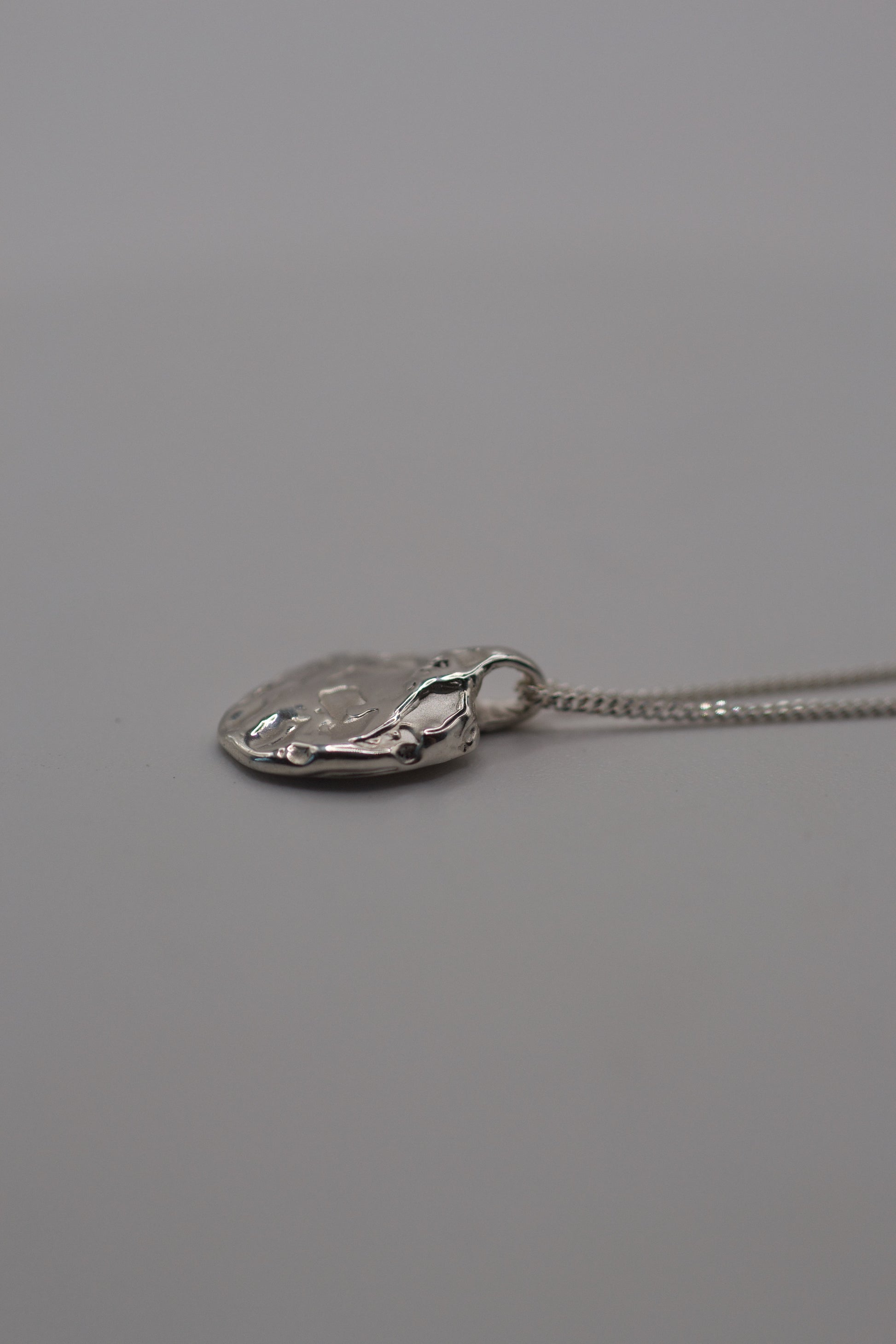 Flat lay photo of a handcrafted molten sterling silver pendant on a delicate chain, featuring organic lost wax textures.