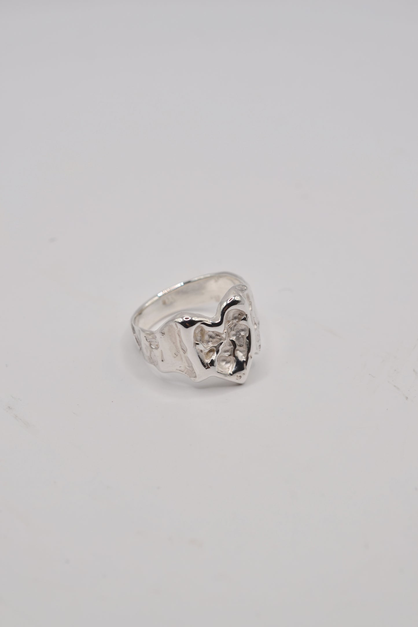 Angled close up of organic lost wax cast ring in sterling silver highlighting molten heart jewellery design