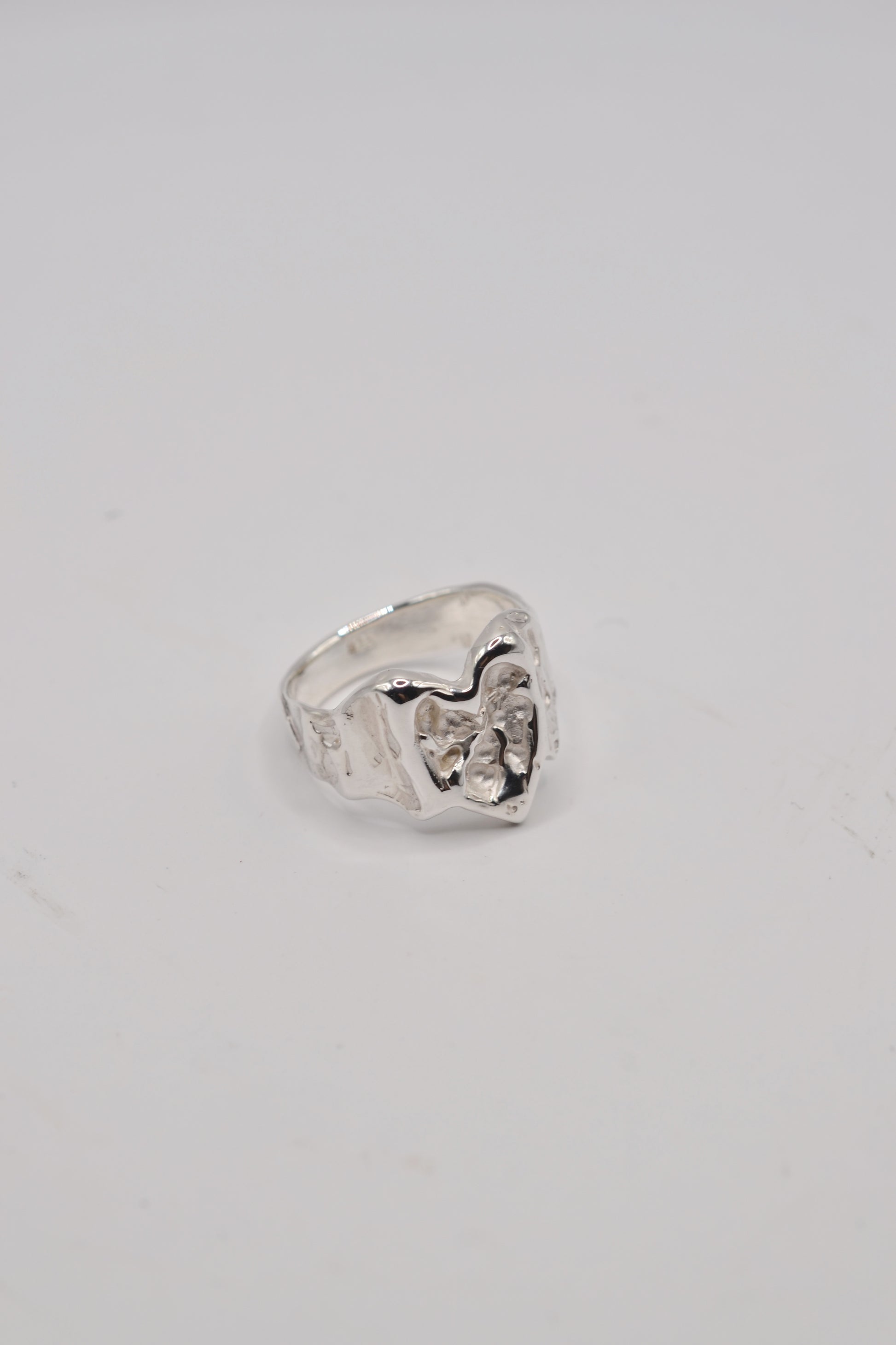 Angled close up of organic lost wax cast ring in sterling silver highlighting molten heart jewellery design
