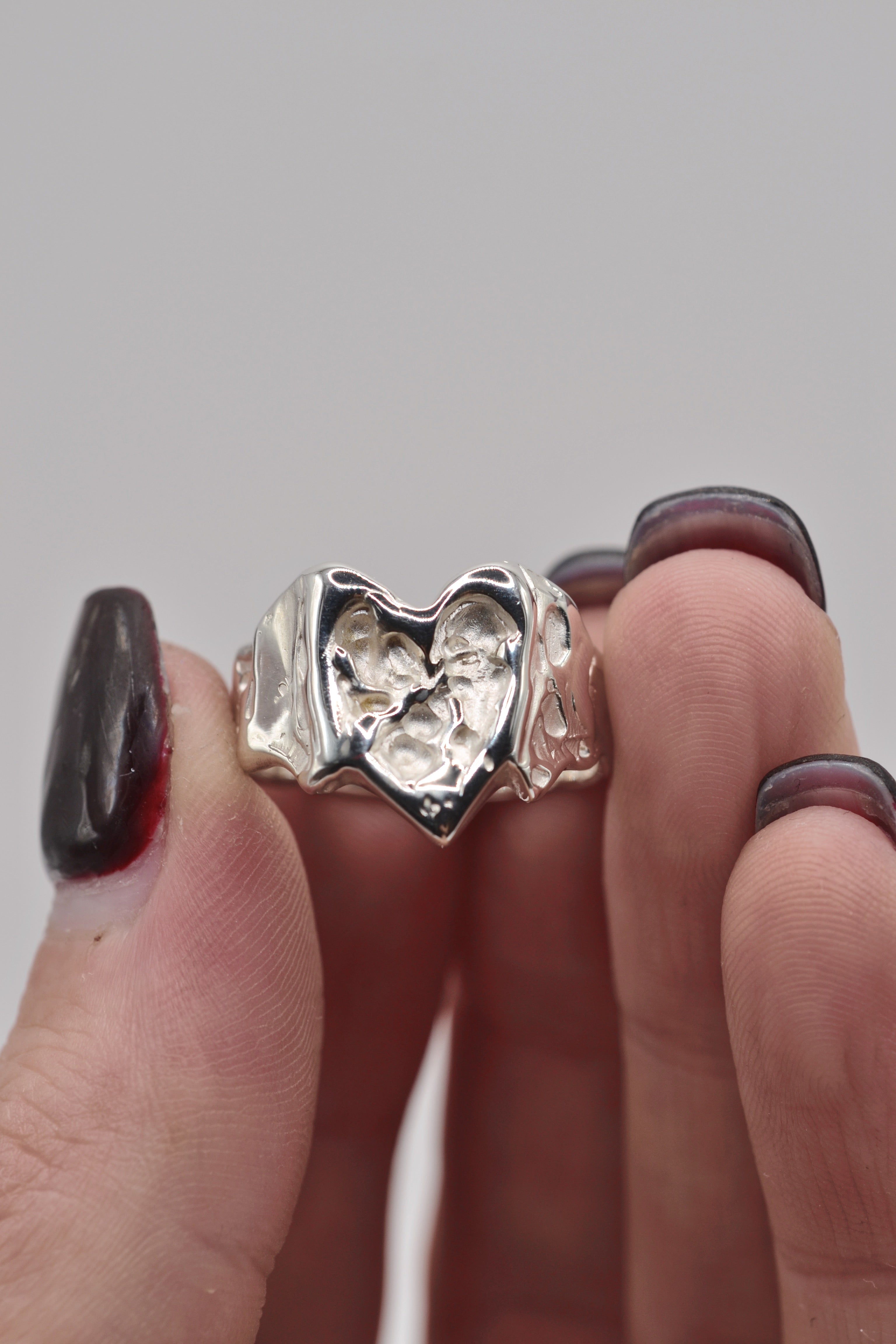 Organic lost wax cast ring held between fingers, sterling silver molten heart jewellery with hand sculpted detail