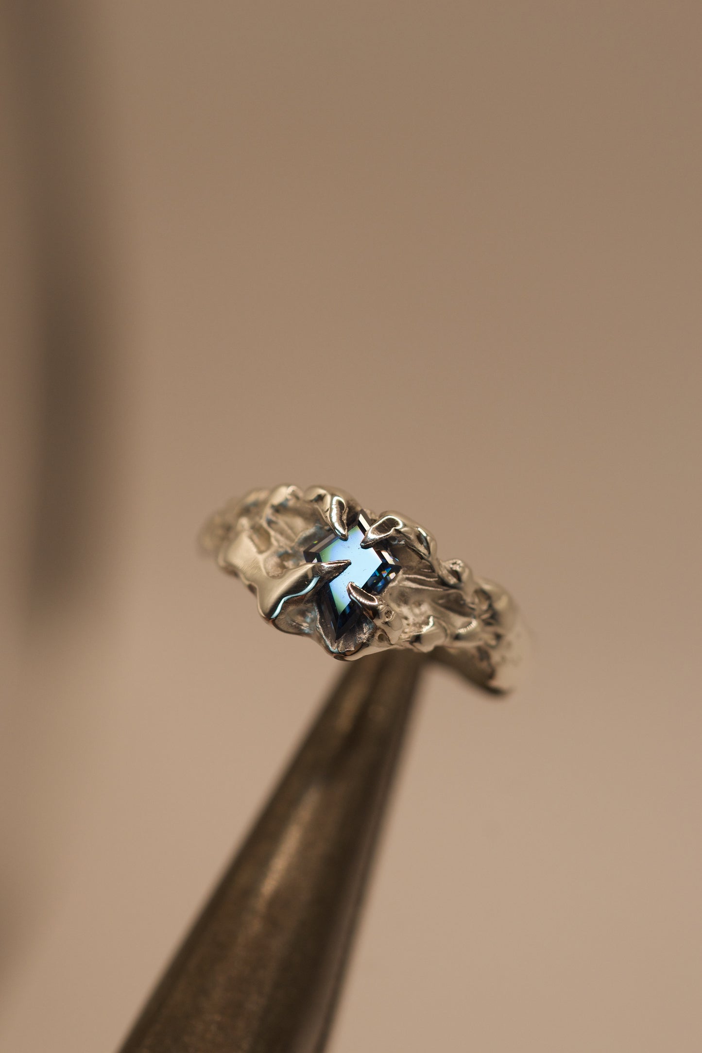 Crafted with the lost wax technique, this handmade sterling silver ring features a bold vivid blue kite cut moissanite set in gothic inspired claws, with molten, organic textures for an alternative style.