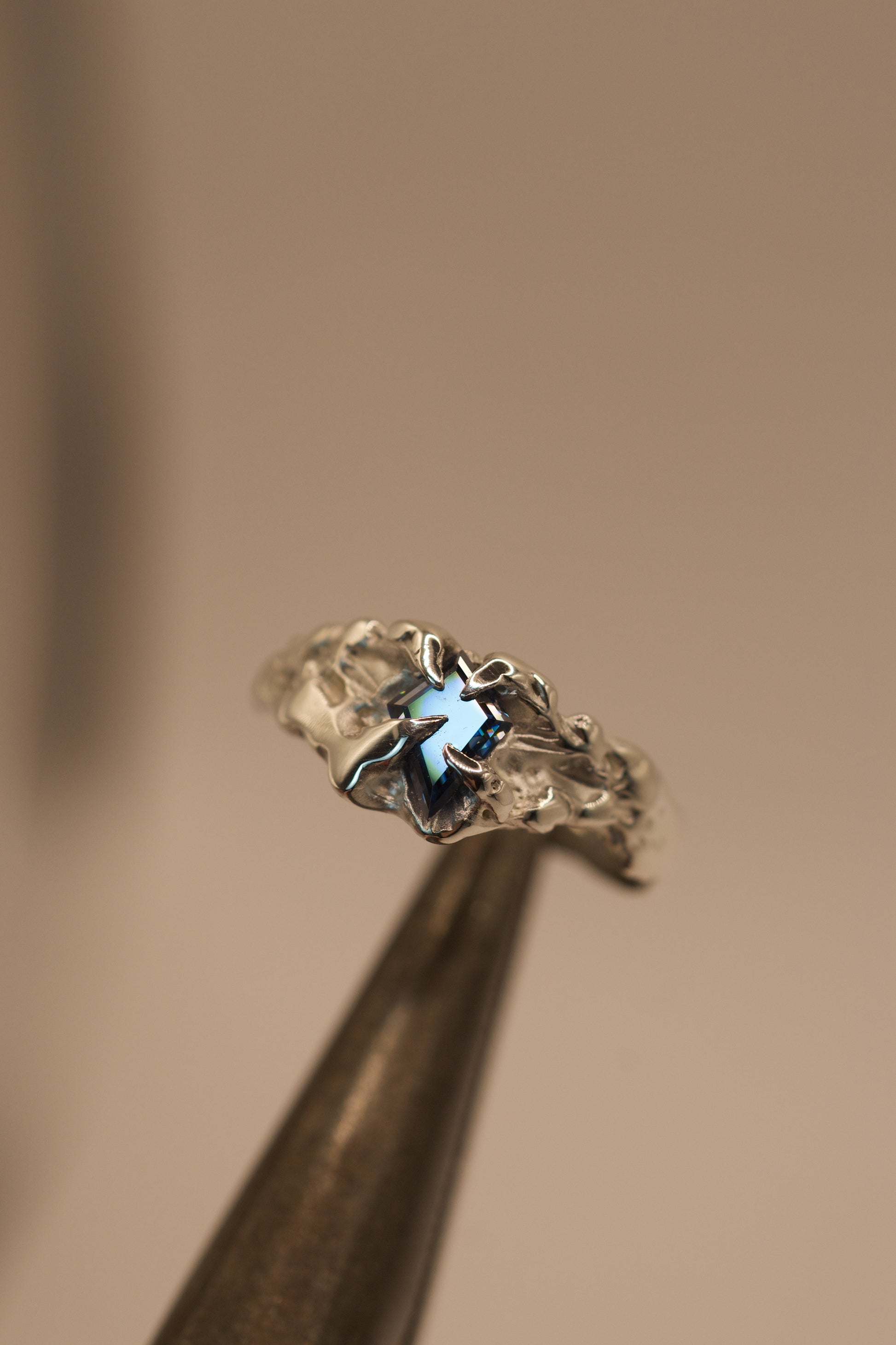 Crafted with the lost wax technique, this handmade sterling silver ring features a bold vivid blue kite cut moissanite set in gothic inspired claws, with molten, organic textures for an alternative style.